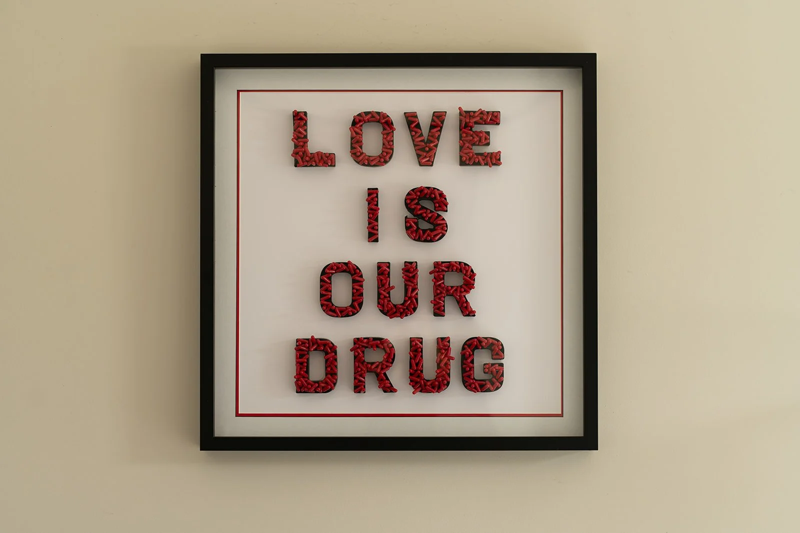 Close up of "LOVE IS OUR DRUG" by Julie Langford, framed contemporary artwork with red pharmaceutical capsules forming the words LOVE IS OUR DRUG