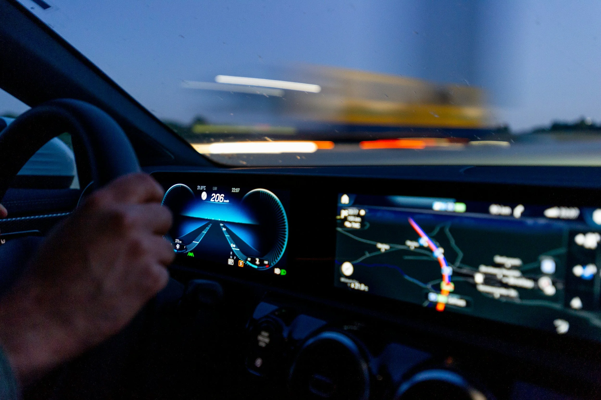 Inside a car at night, the dashboard displays a speed of 206 mph, and the view through the windshield shows blurred lights and a dark sky, indicating high speed driving.