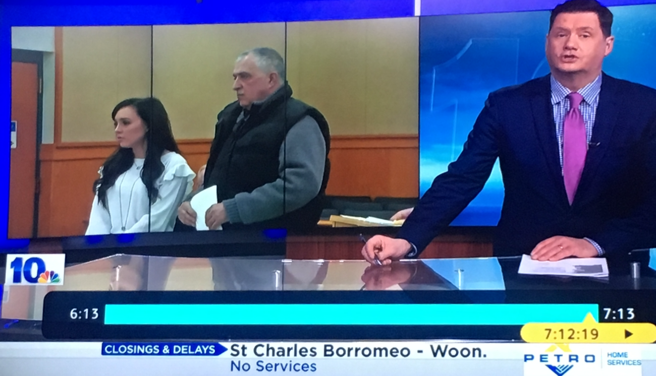 Television news anchor reporting with a large screen behind showing a courtroom scene with two people and a judge or lawyer, NBC 10 logo on the bottom left, news ticker at the bottom, and clock showing 6:13.