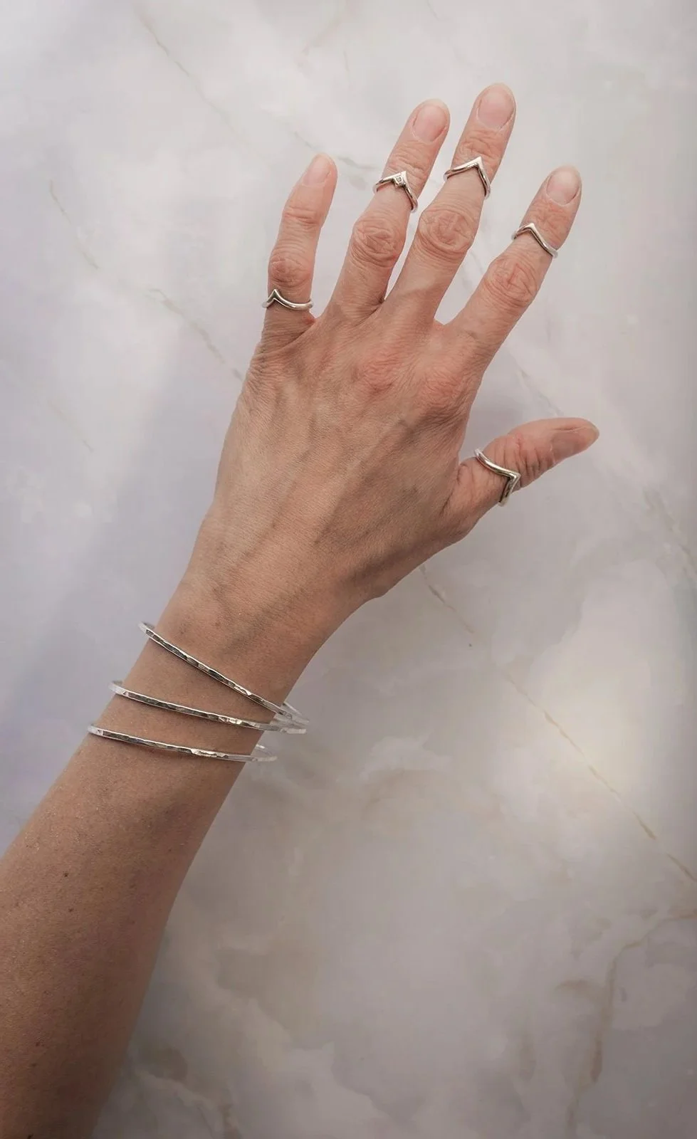 Een hand  met meerdere zilveren sieraden, waaronder verschillende zilveren ringen en drie bangles, cirkelvormige zilveren armbanden.