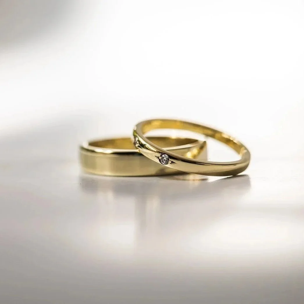 Twee gouden ringen, een met twee kleine diamanten, liggen op een witte ondergrond.