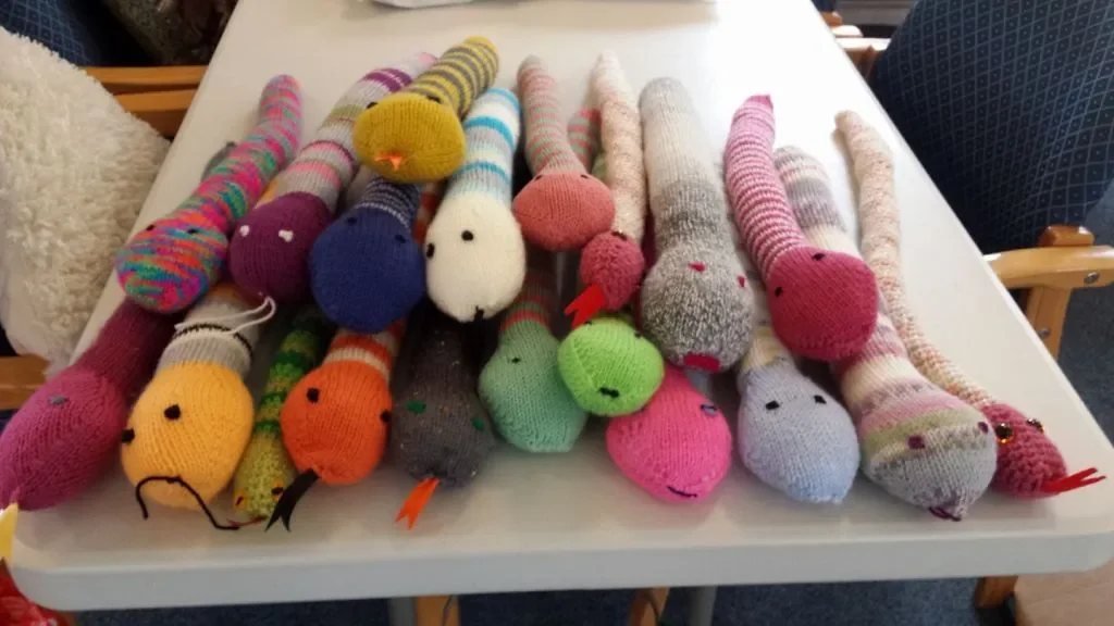 Colorful, knitted sock animals with faces, arranged on a white table.