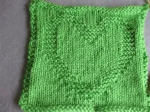 Green knitted square with a heart pattern at the center.