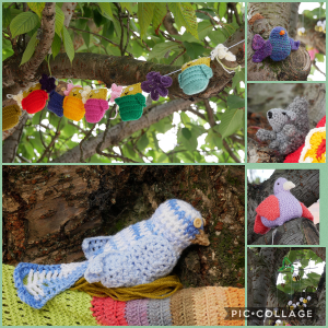 Colorful handmade crochet animals and decorations hanging on a tree branch, including a purple octopus, a green and pink turtle, a gray mouse, a pink and gray bird, and a blue bird with yellow beak, with a large crocheted owl sitting on a tree trunk below.
