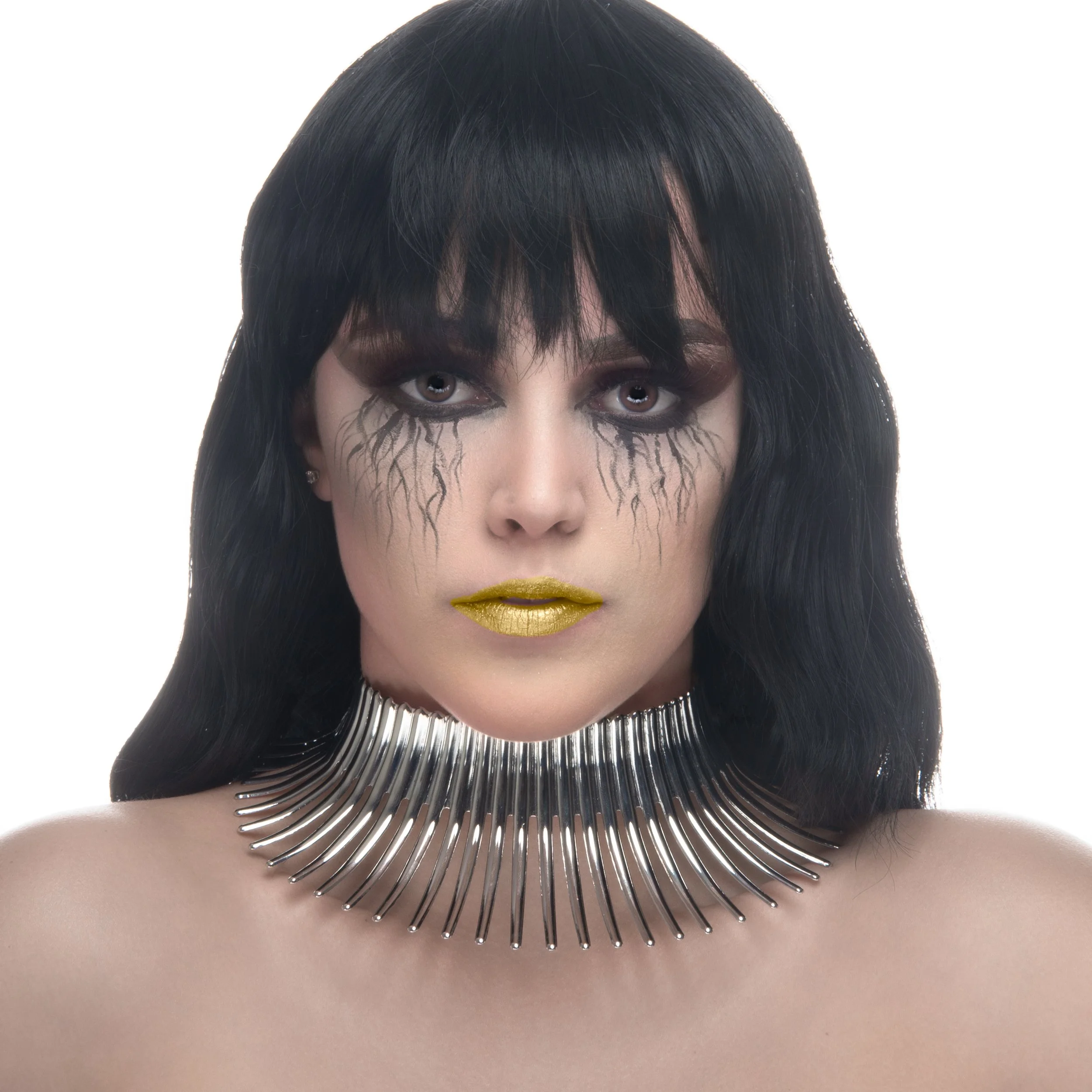A person with long black hair and makeup, wearing a metallic choker necklace, and a shiny, spiky silver collar around the neck.