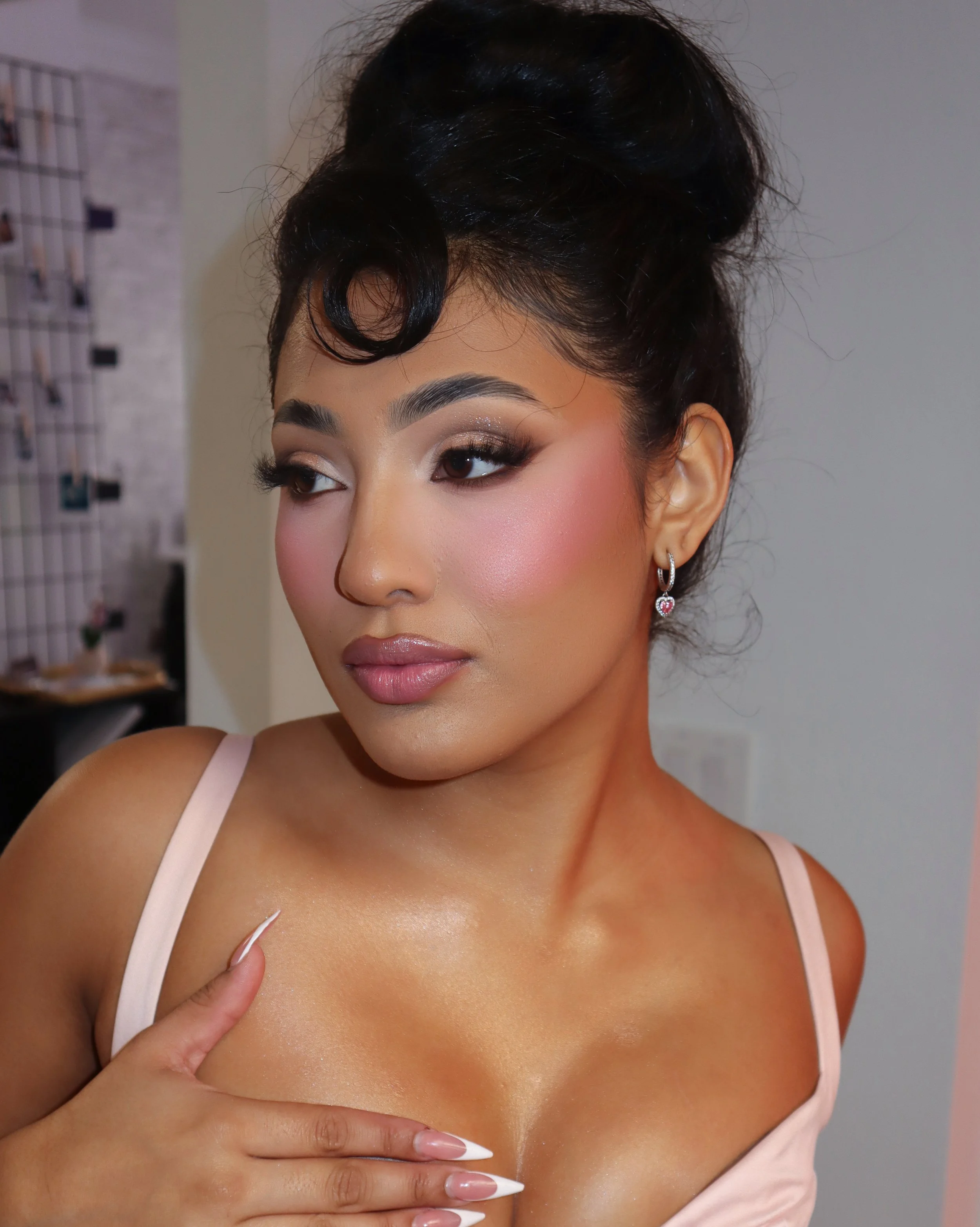 Close-up of a woman with styled dark hair, makeup, and a white satin camisole, touching her shoulder.
