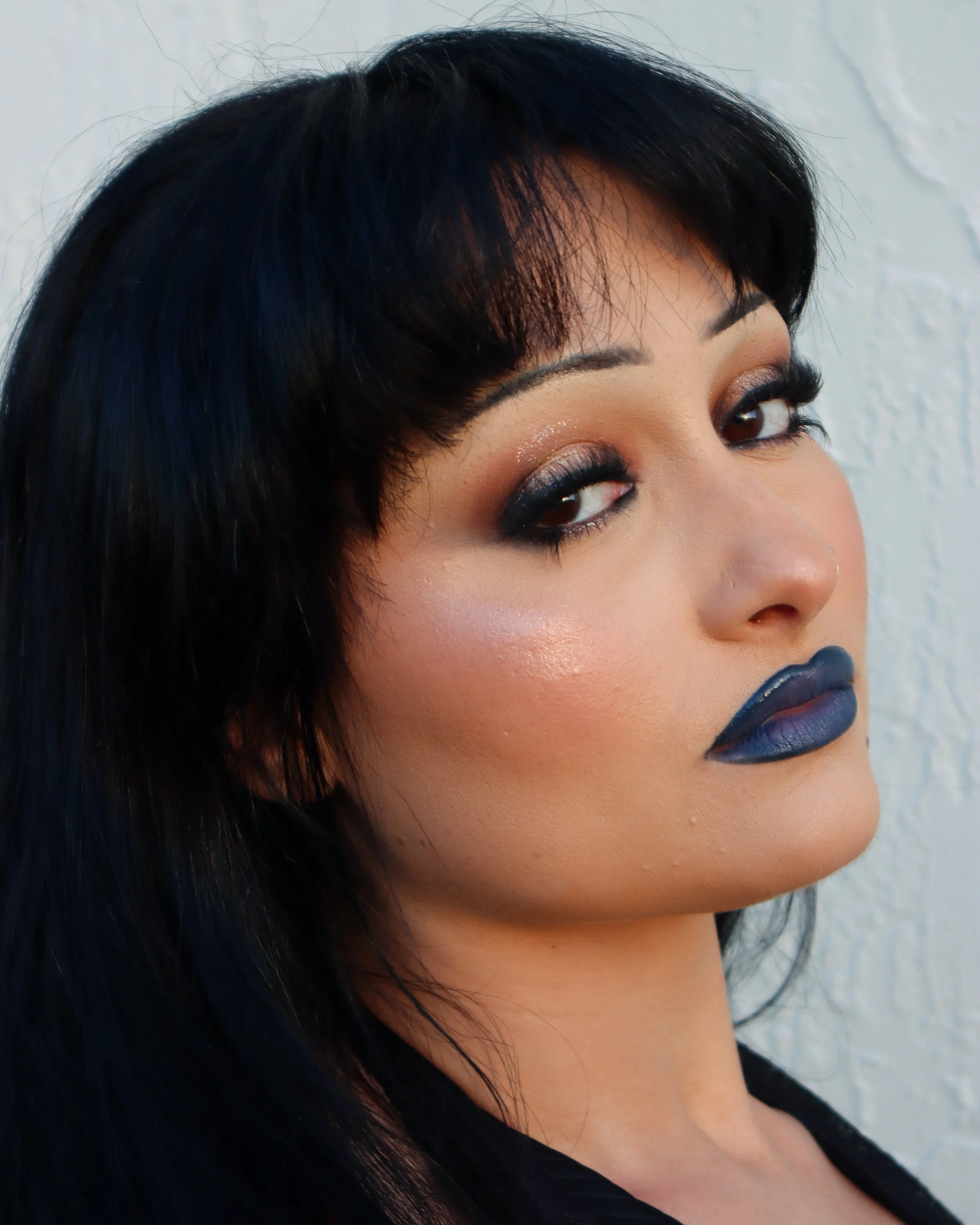 Close-up of a woman's face showing her eyes, nose, and lips with makeup, against a plain light-colored background.