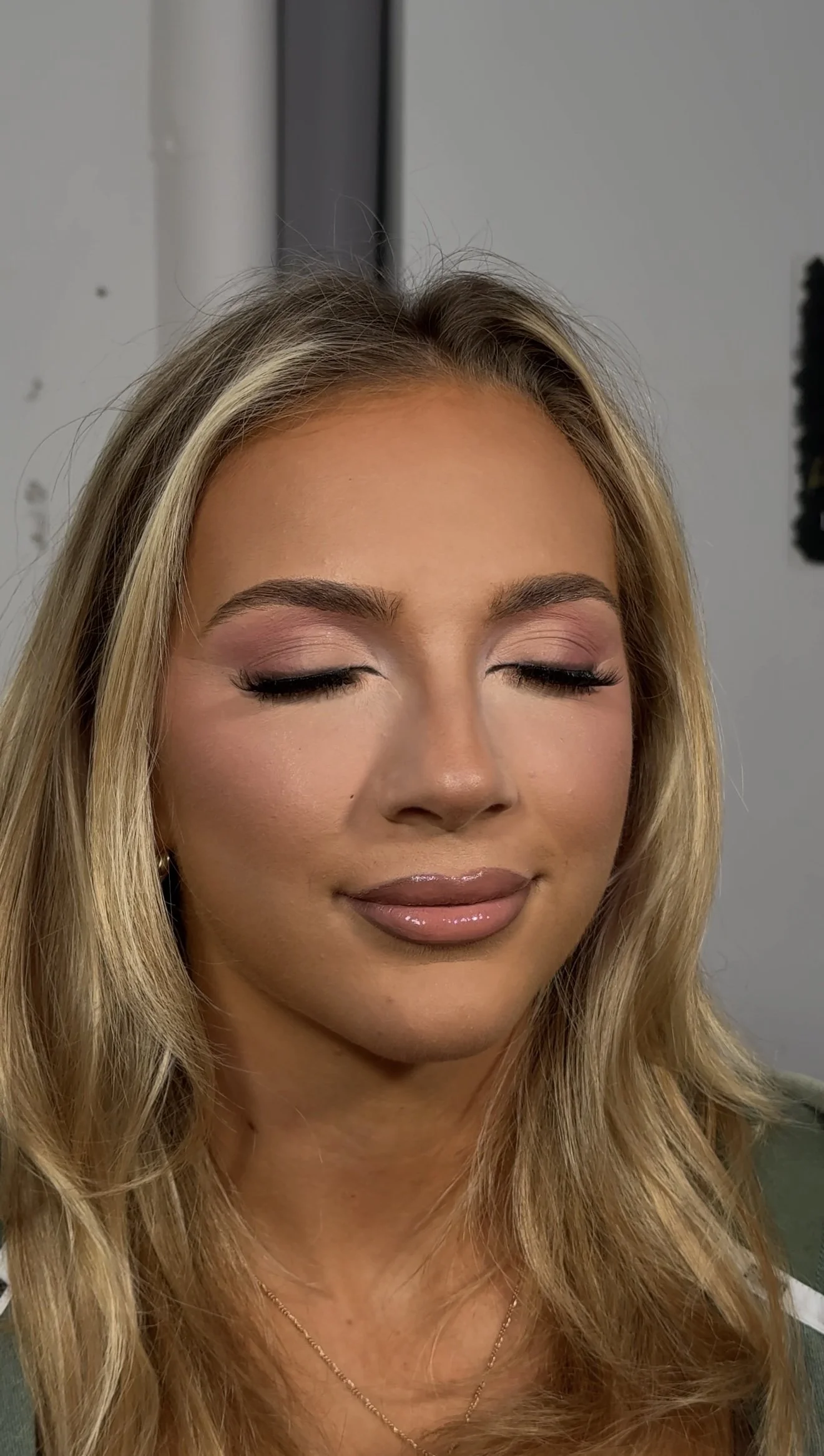 A woman with blonde hair, closed eyes, wearing makeup, and a gold necklace.