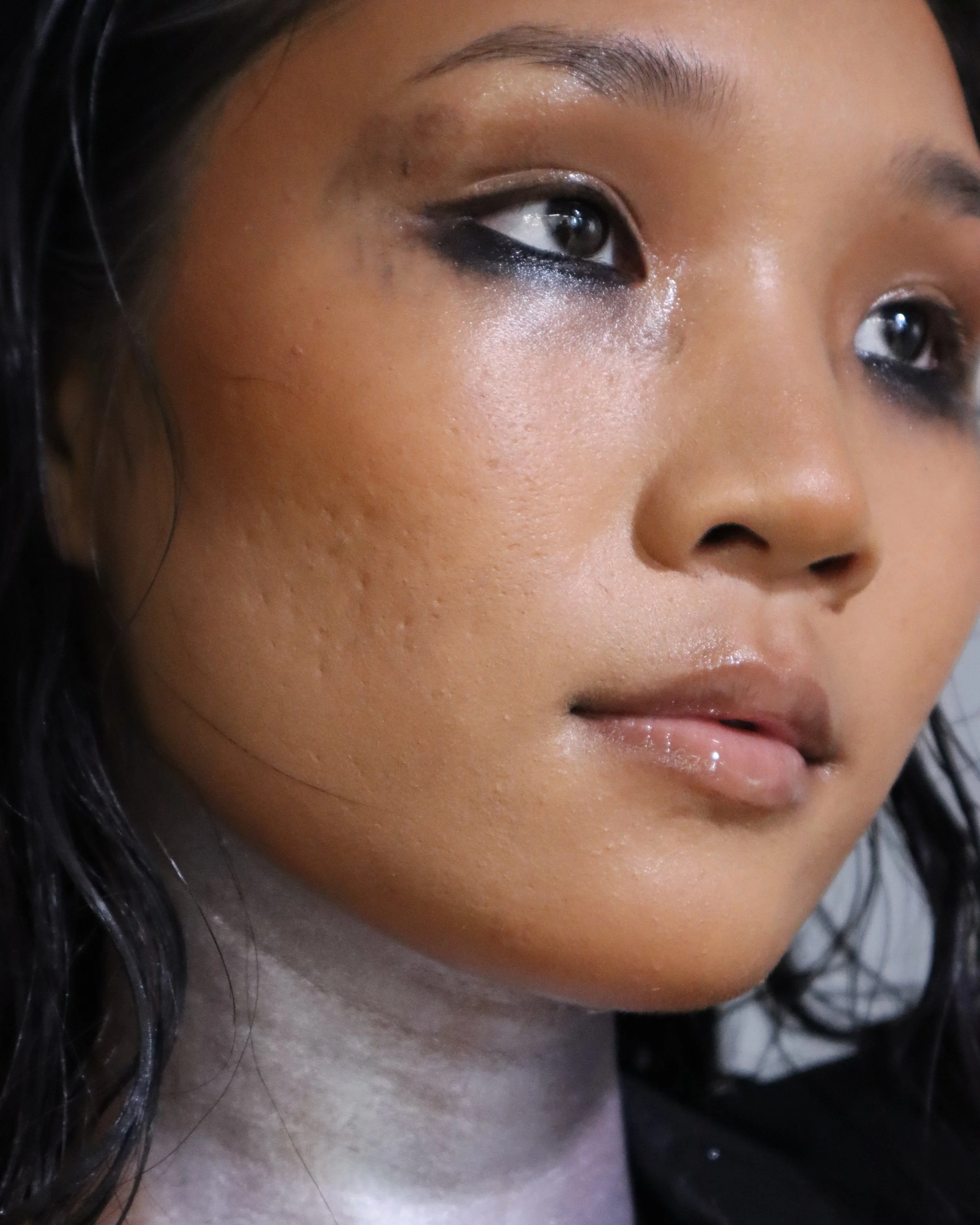 Close-up of a woman's face with black eyeliner and eyeshadow, showing a natural skin tone and shiny lips.