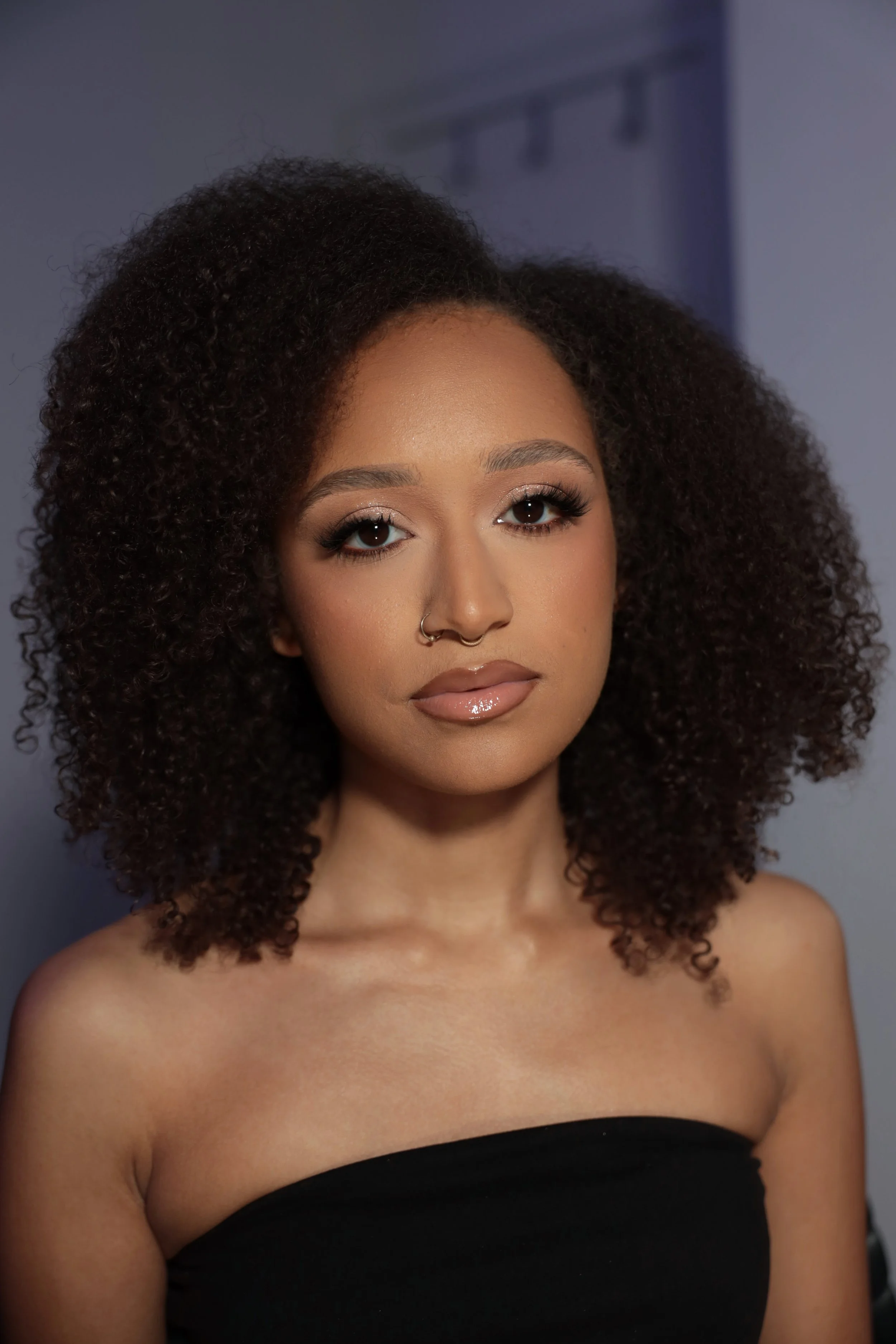 A woman with dark brown, curly hair wearing a strapless black top.