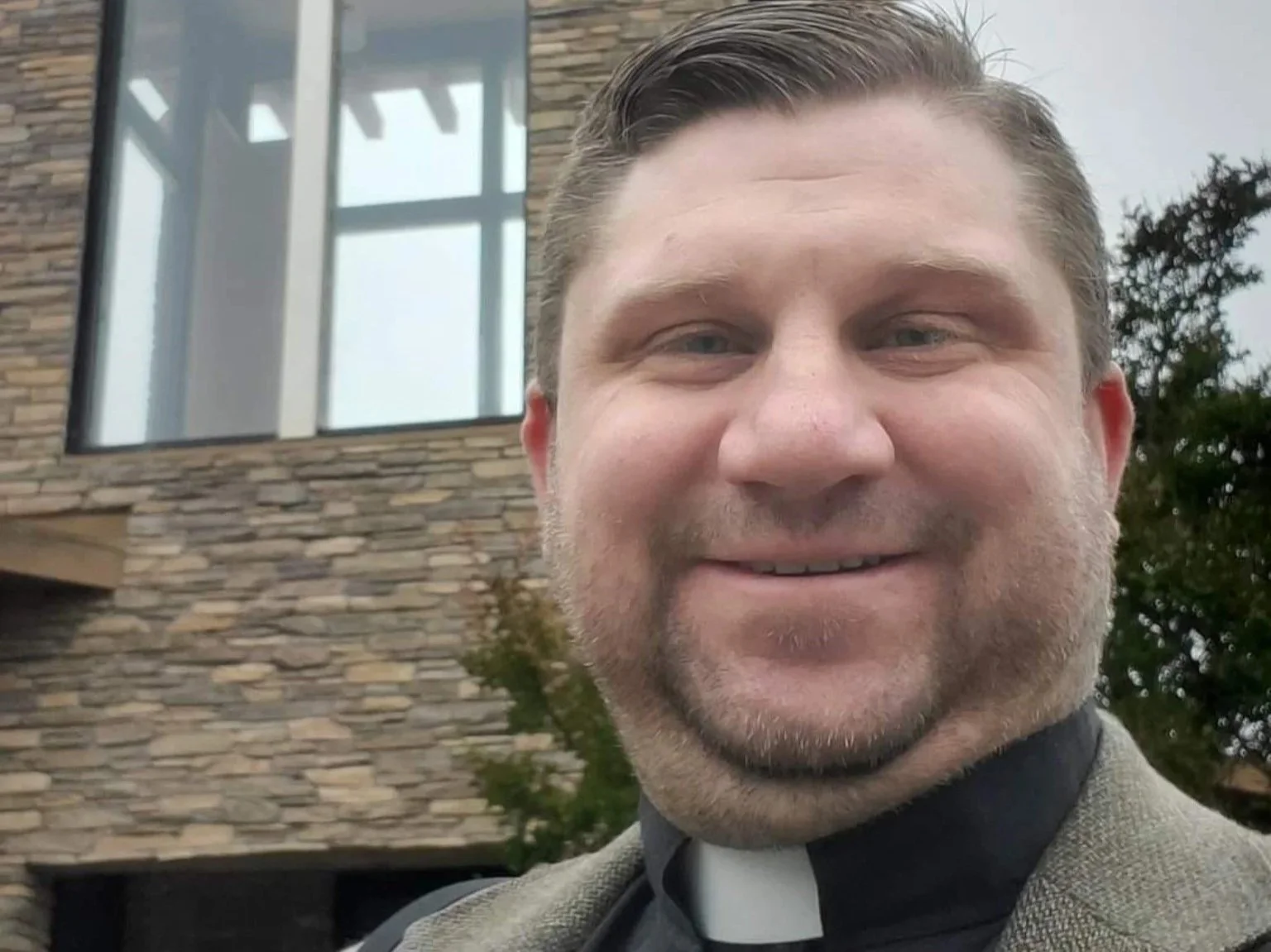 Brian Brozovic wearing a clerical collar outside a church building.