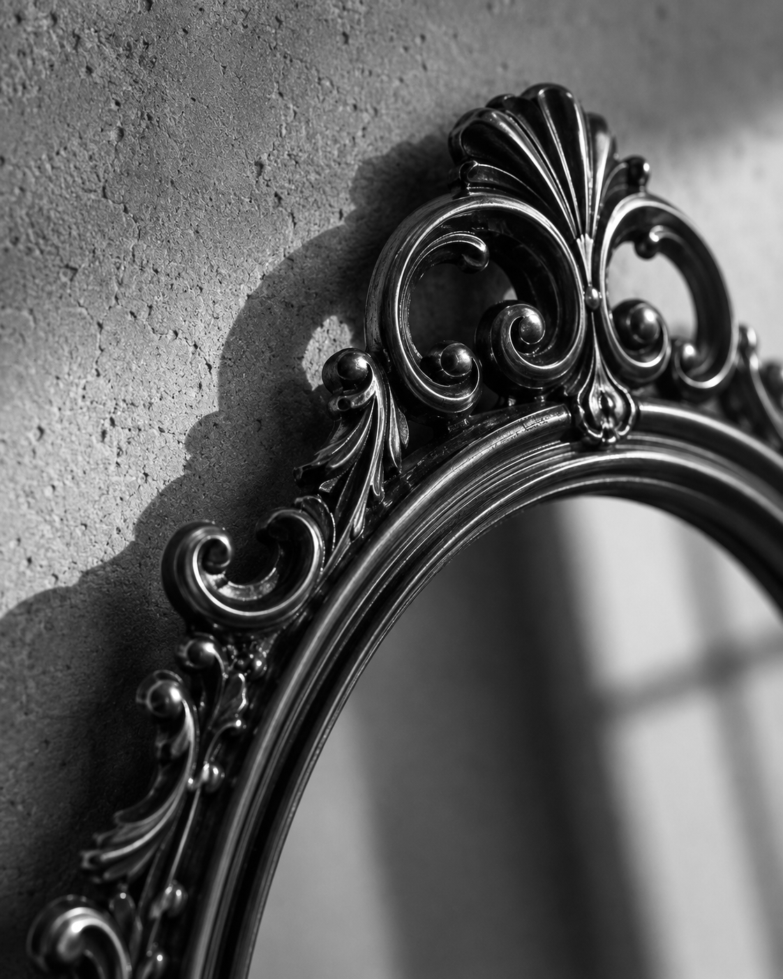 Black-and-white close-up of an ornate mirror frame casting a shadow on the wall