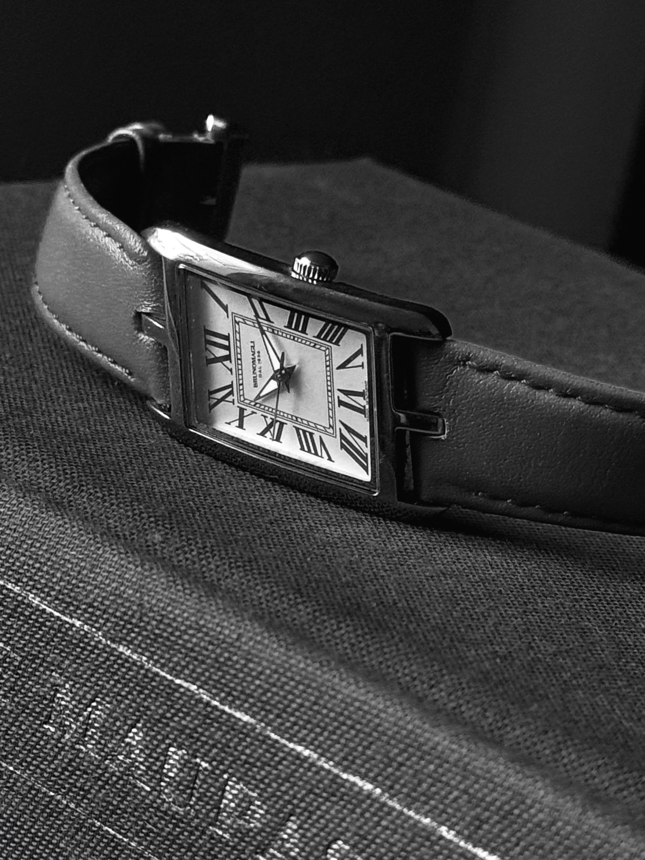 Black-and-white photograph of a rectangular wristwatch with Roman numerals and a leather strap resting on a book.