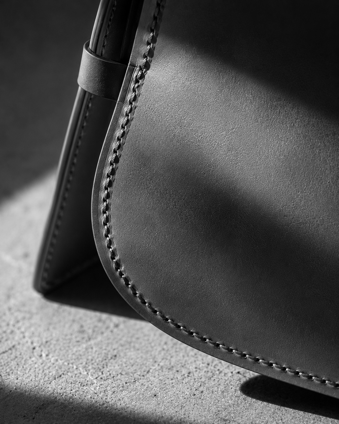 Black-and-white close-up photograph of a structured leather handbag with visible stitching