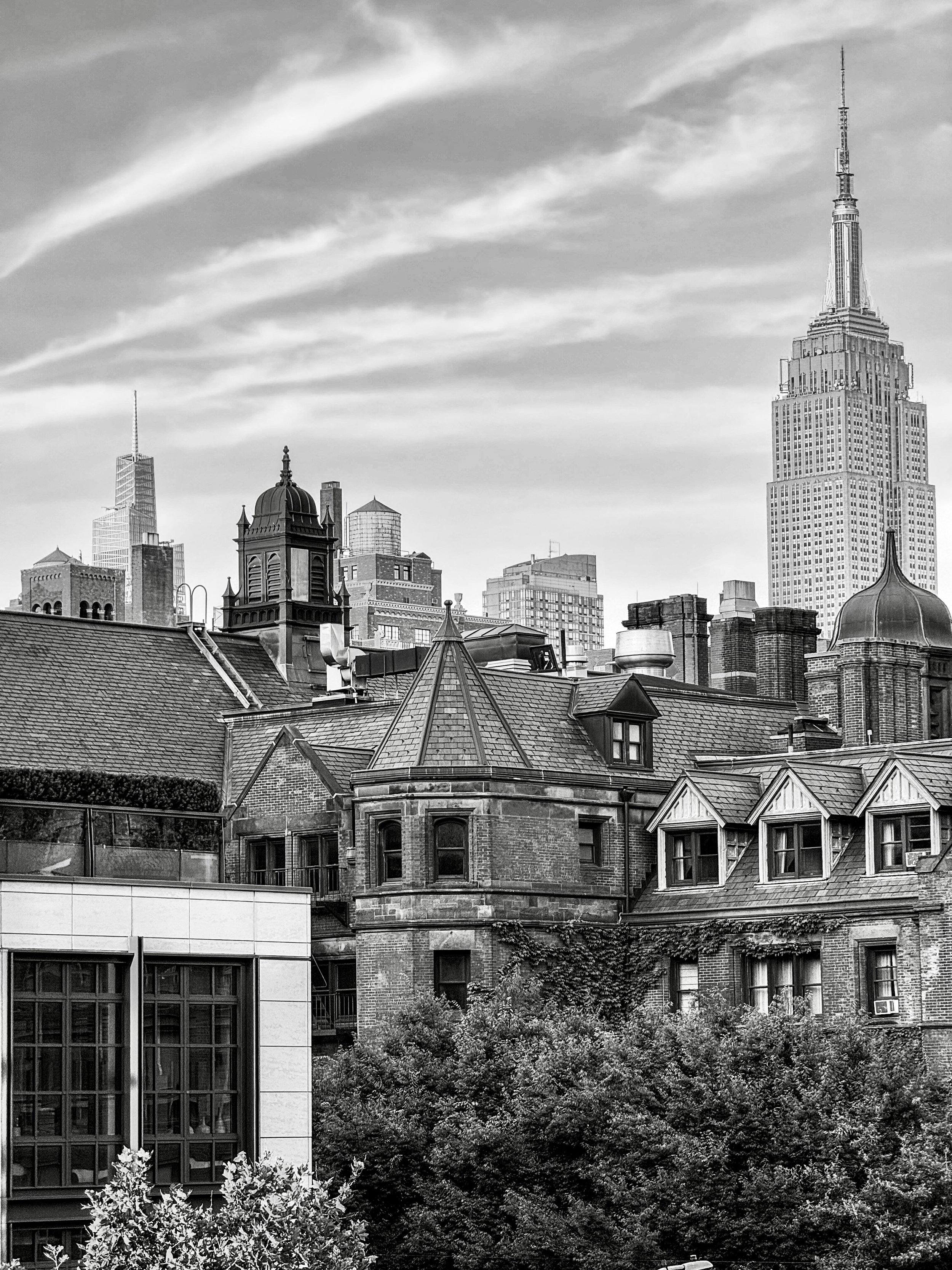 Black-and-white photograph of the Manhattan skyline viewed from the High Line, with the Empire State Building rising above historic rooftops