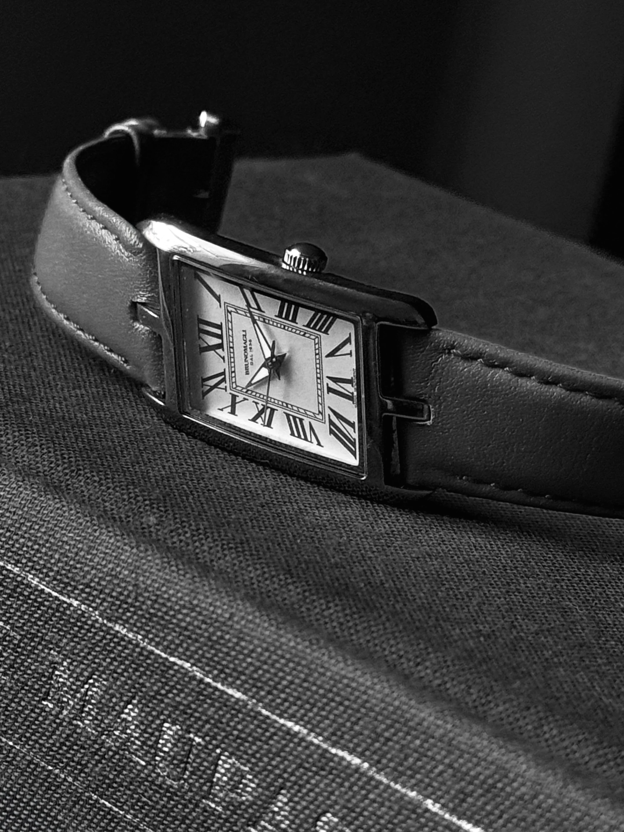 Black-and-white photograph of a rectangular wristwatch with Roman numerals and a leather strap resting on a book.