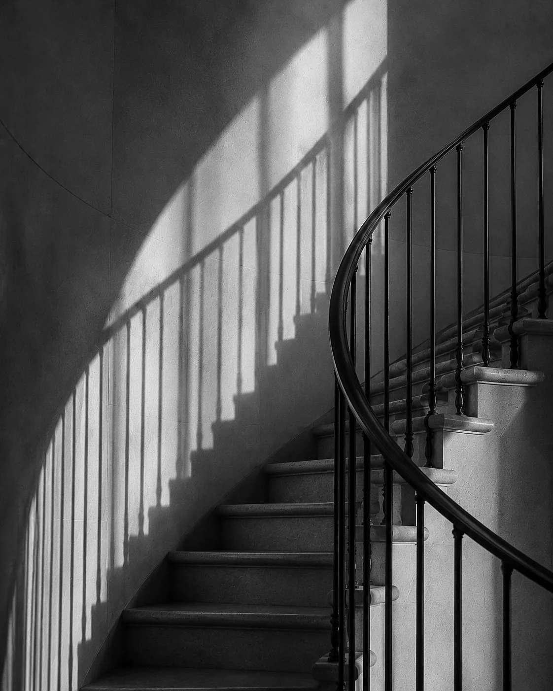 Black-and-white photograph of a curved staircase casting geometric shadows on the wall