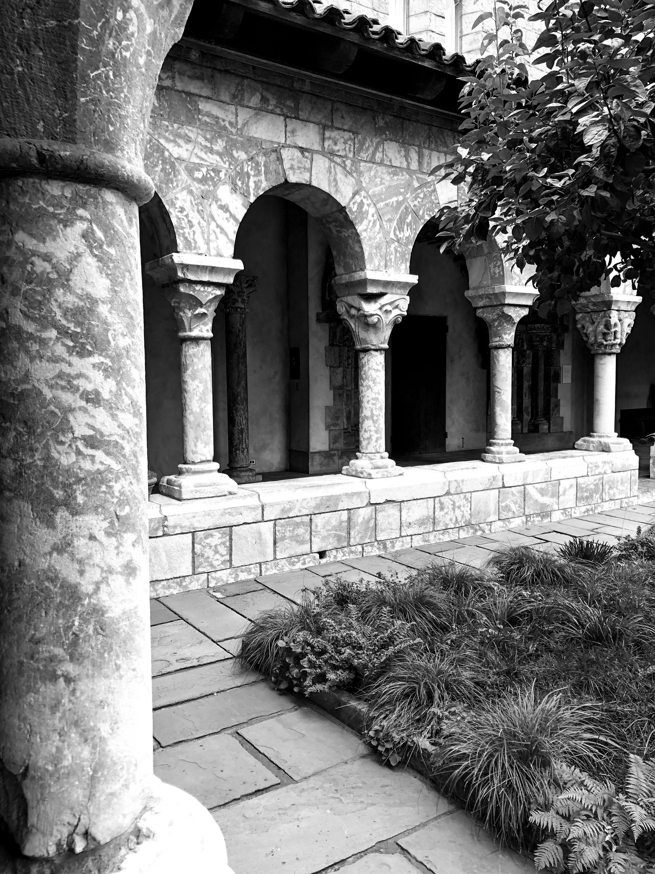 Black-and-white photograph of the Cuxa Cloister at The Met Cloisters, with stone columns and arched walkways surrounding a garden