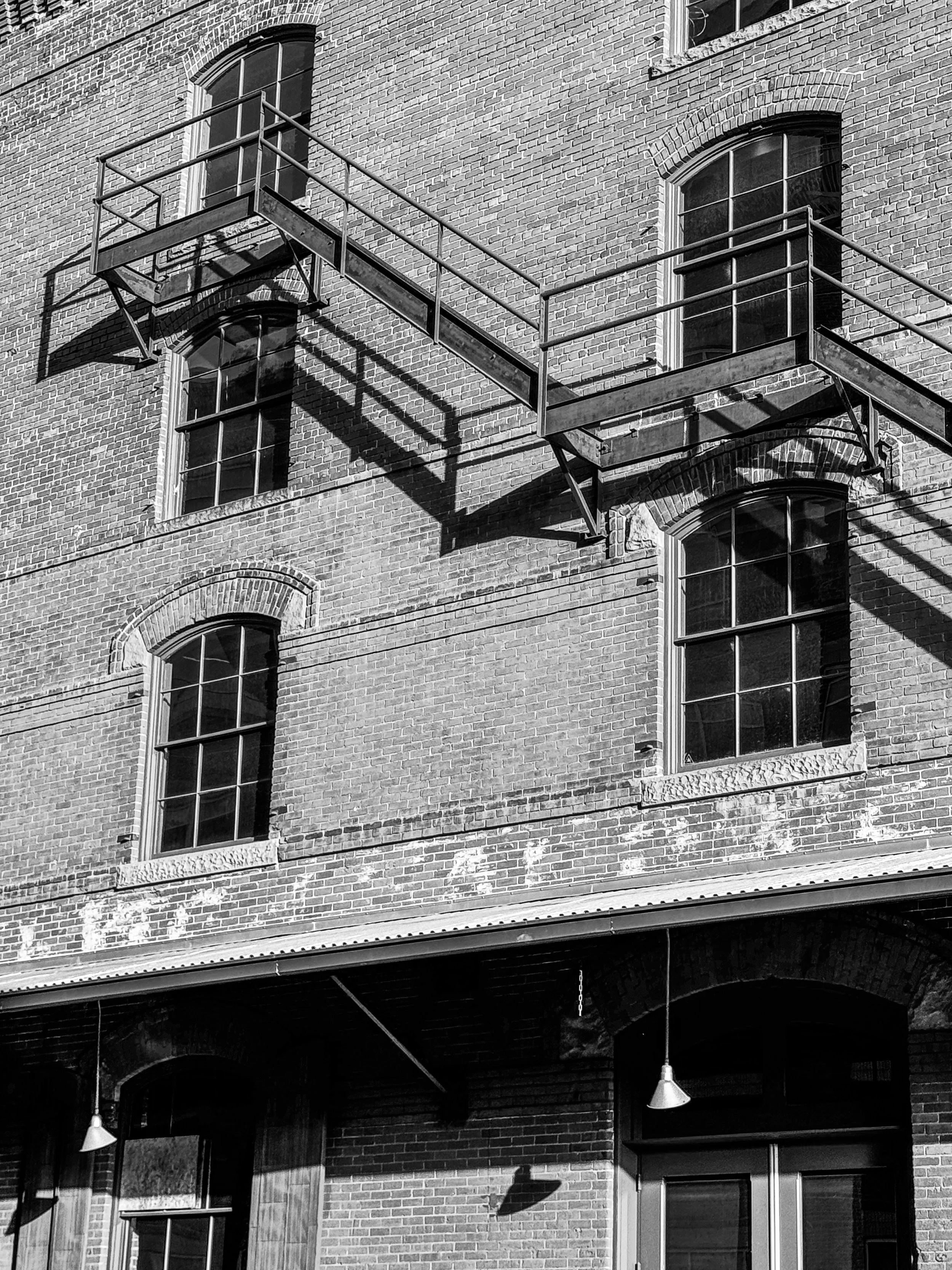Black-and-white photograph of an old brick industrial building with exterior metal fire escapes in Denver, Colorado