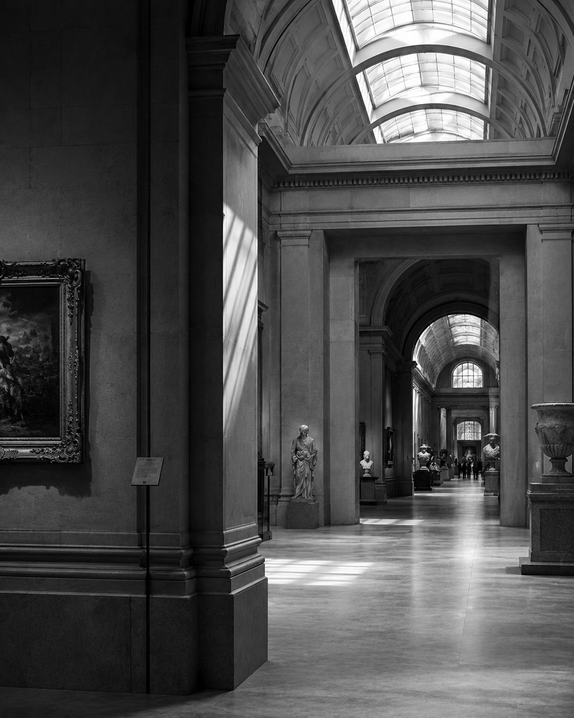 Black-and-white photograph of a grand museum gallery with vaulted skylights and a series of arched doorways