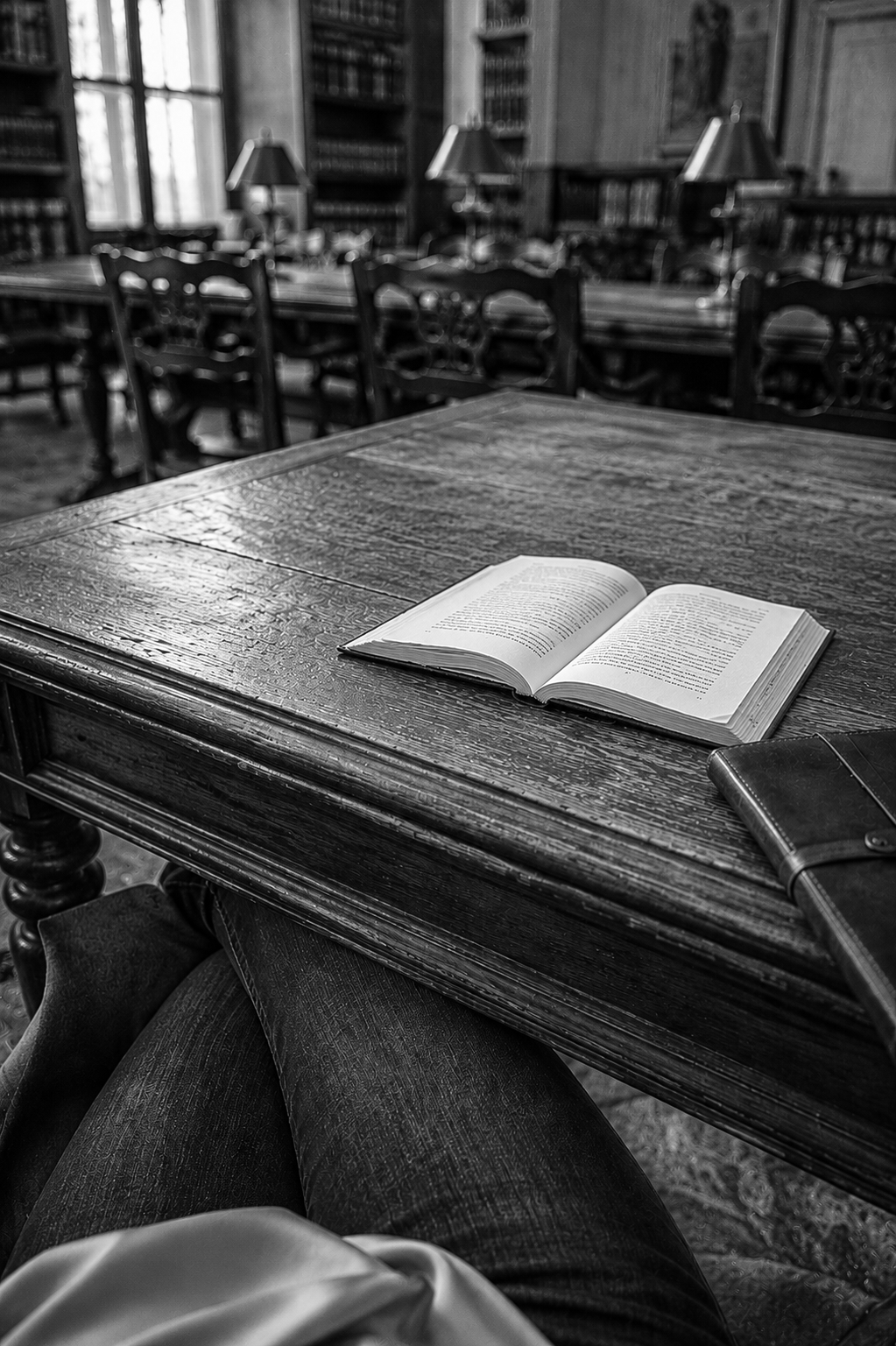 Black-and-white photograph of an open book resting on a wooden table in a reading room