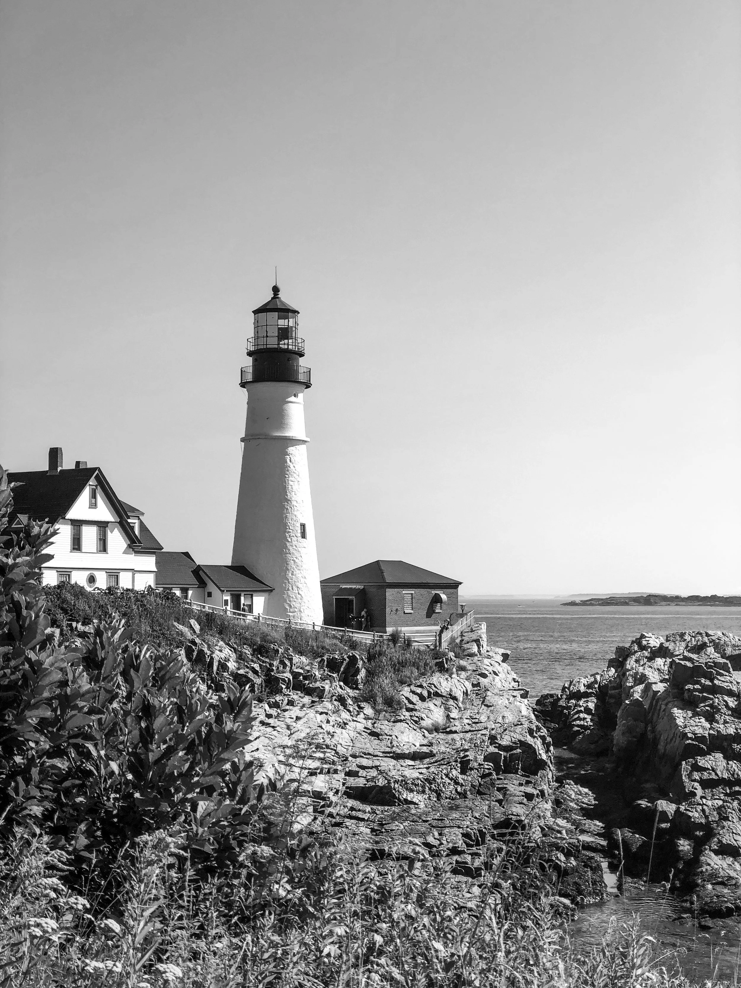 Black-and-white photograph of a lighthouse on the rocky Maine coast overlooking the ocean