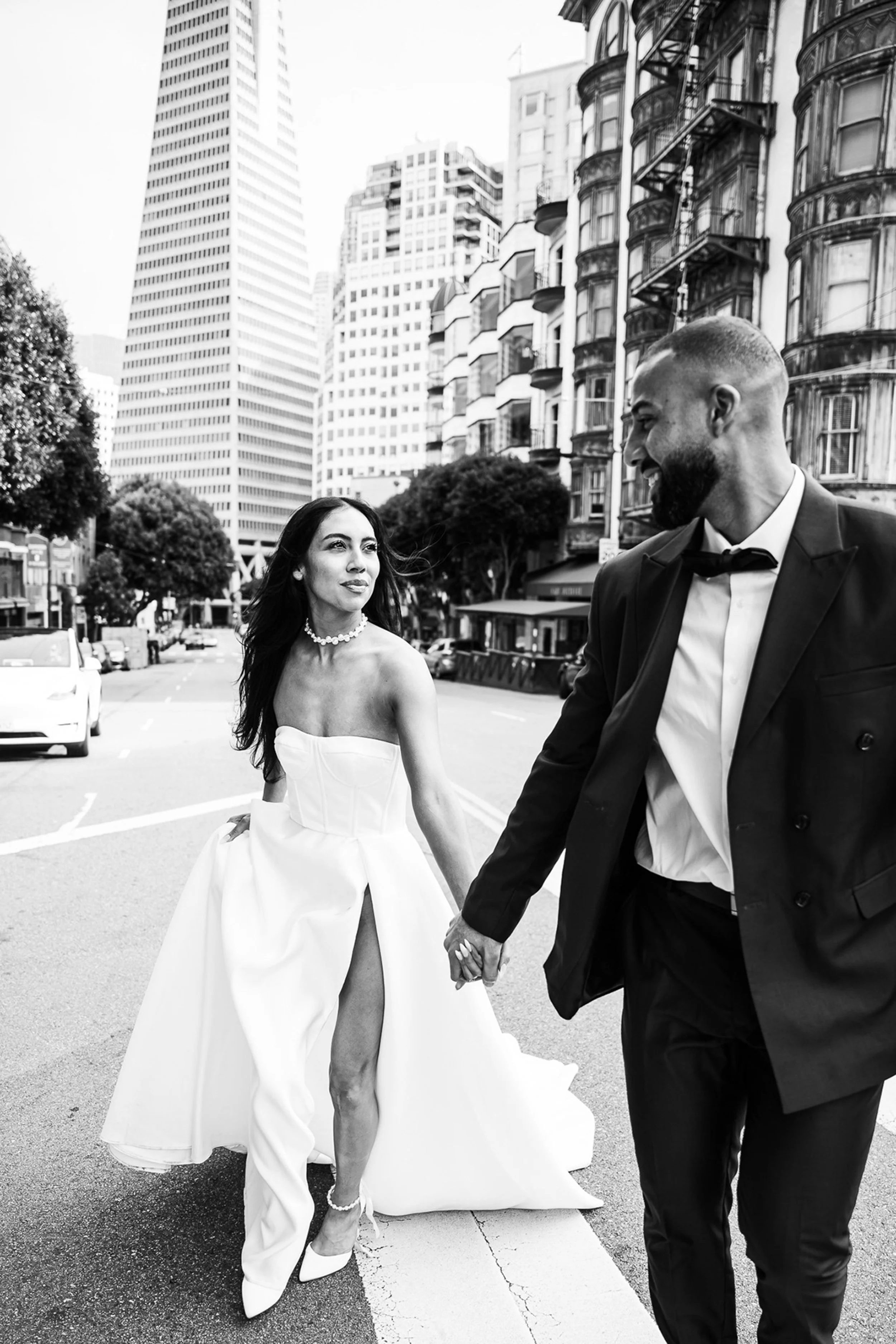 Bride and groom crossing the street in front of Transamerica Building in downtown San Francisco.