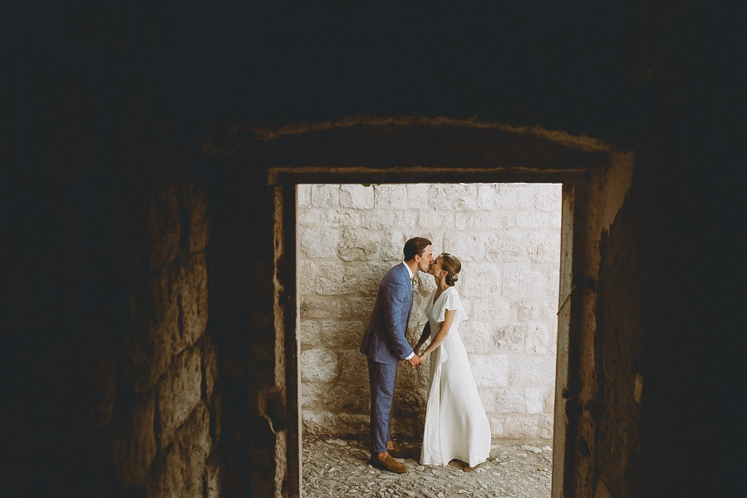 A bride and groom standing and kissing in a natural stone archway in the Bay Area.