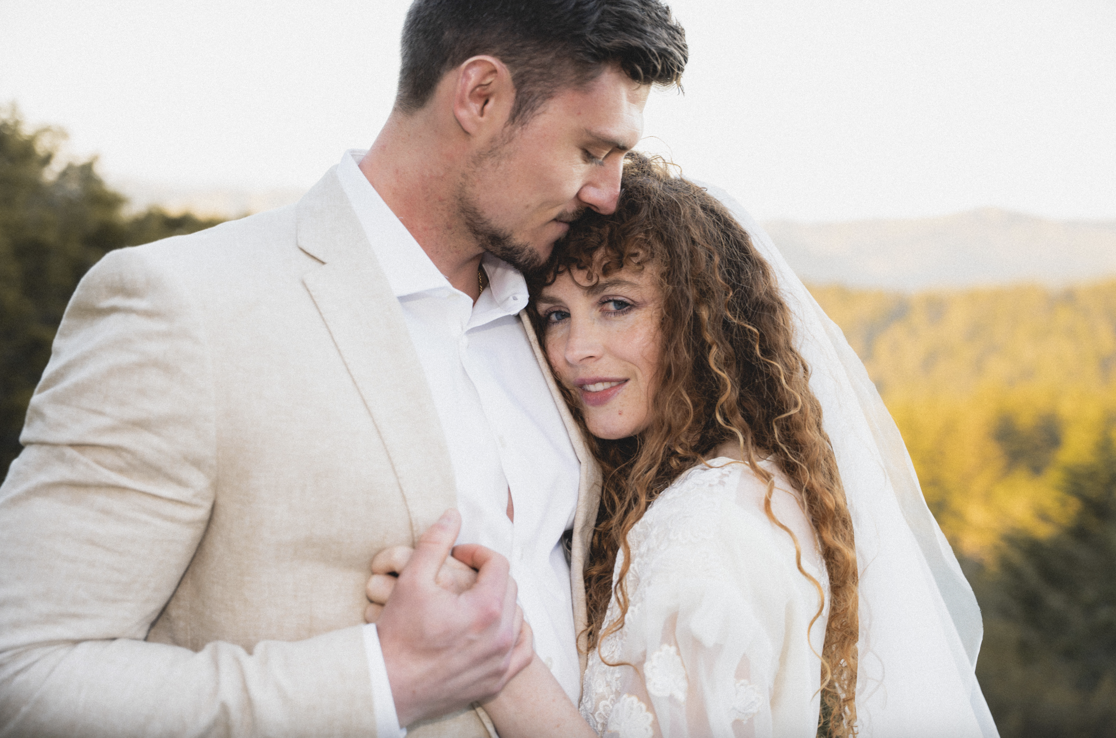 A man and a woman are hugging outdoors, with the man resting his forehead on the woman's head and the woman looking into the camera. Elopement photography in Mt Tamalpais, Marin County, Northern California.