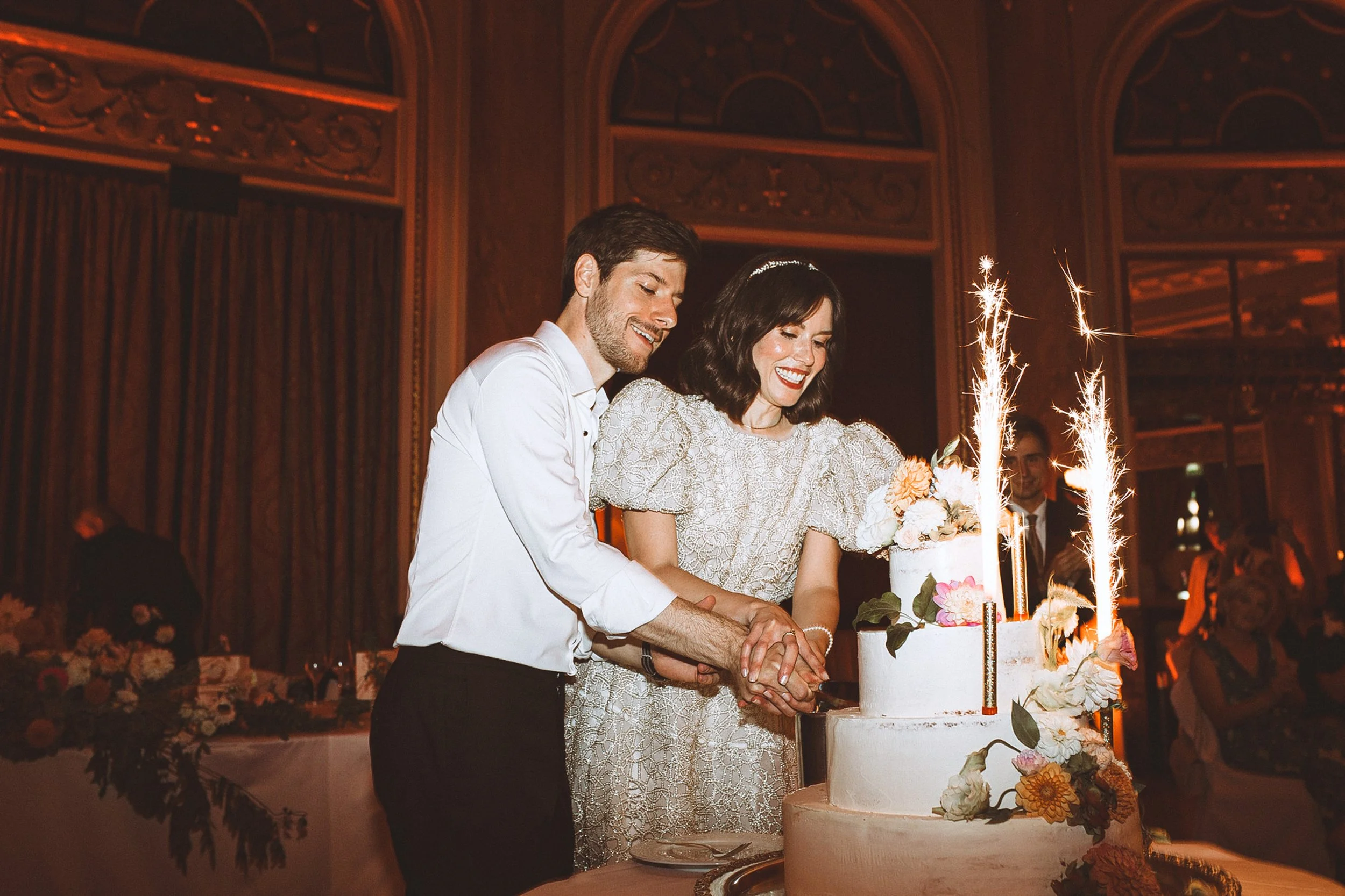 Newlyweds cutting their wedding cake with sparklers at a Bay Area reception, bride in a lace dress, flash night wedding photography.