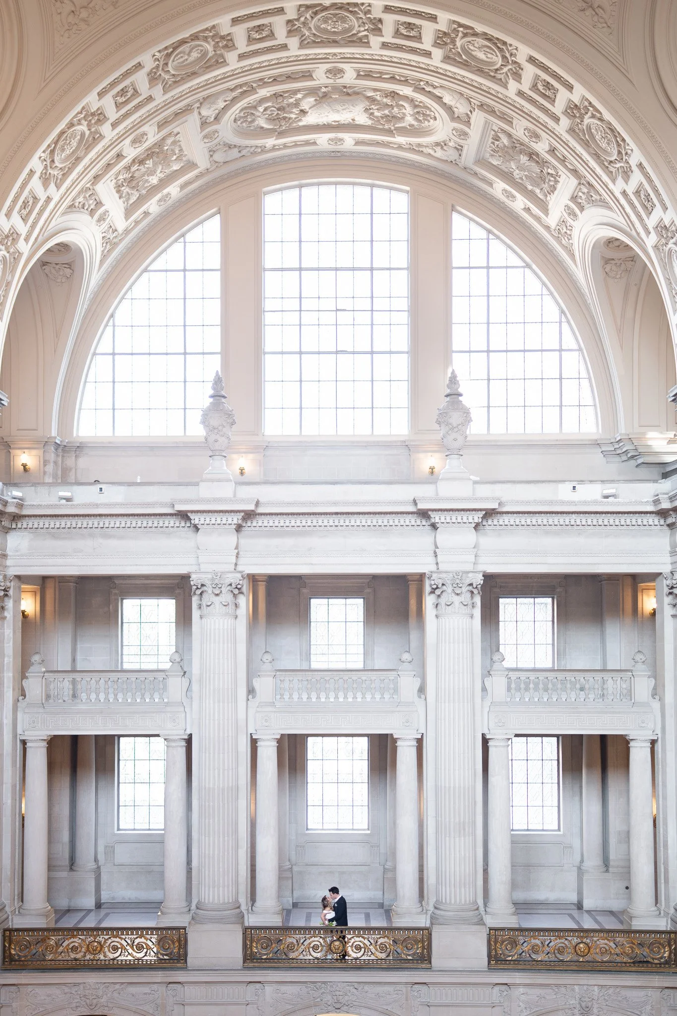 Couple embracing on a balcony inside San Francisco City Hall's rotunda.