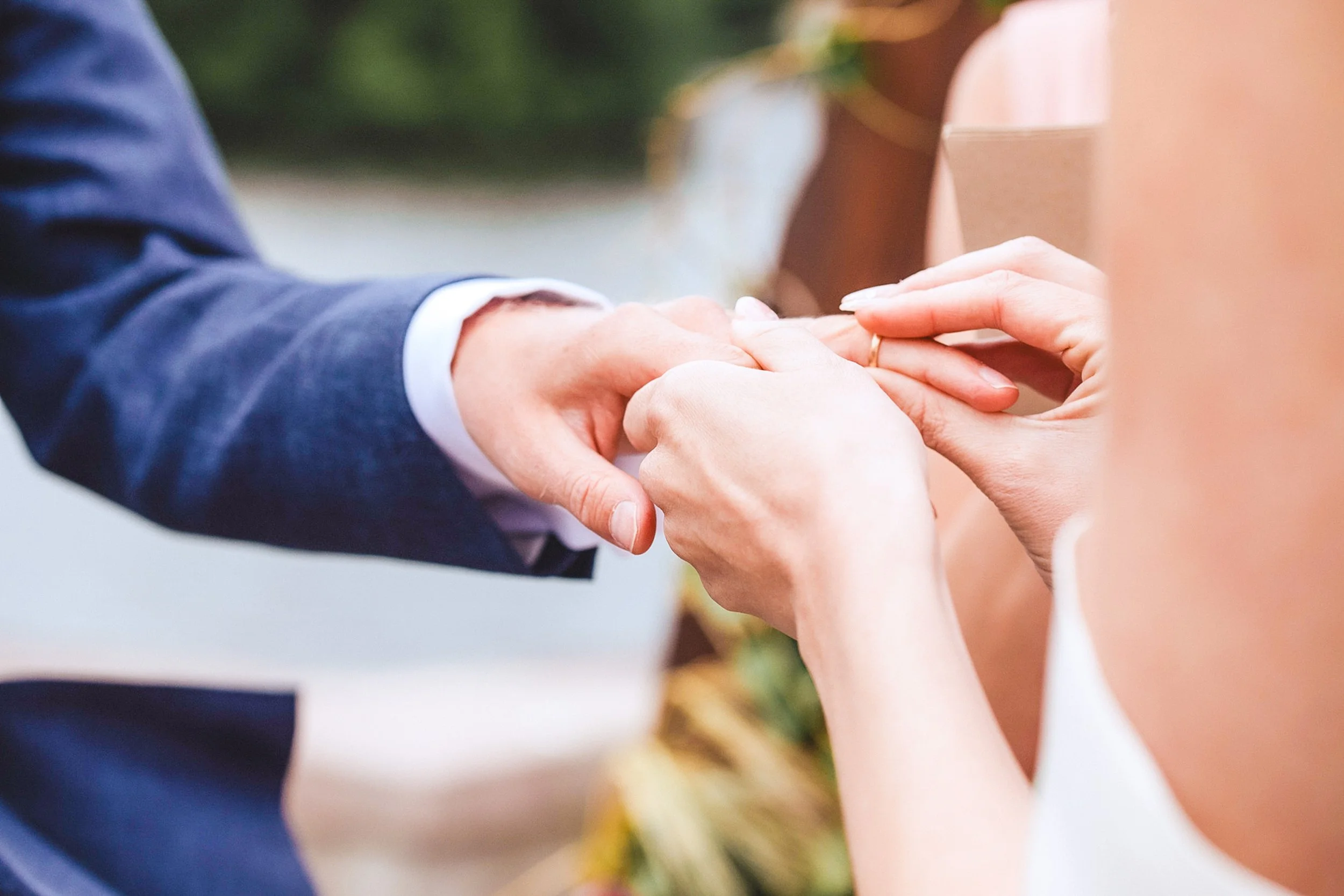A couple holding hands, with the woman's hand being placed over the man's hand, during a wedding ceremony, with a blurred outdoor background in the backyard wedding in Bay Area.
