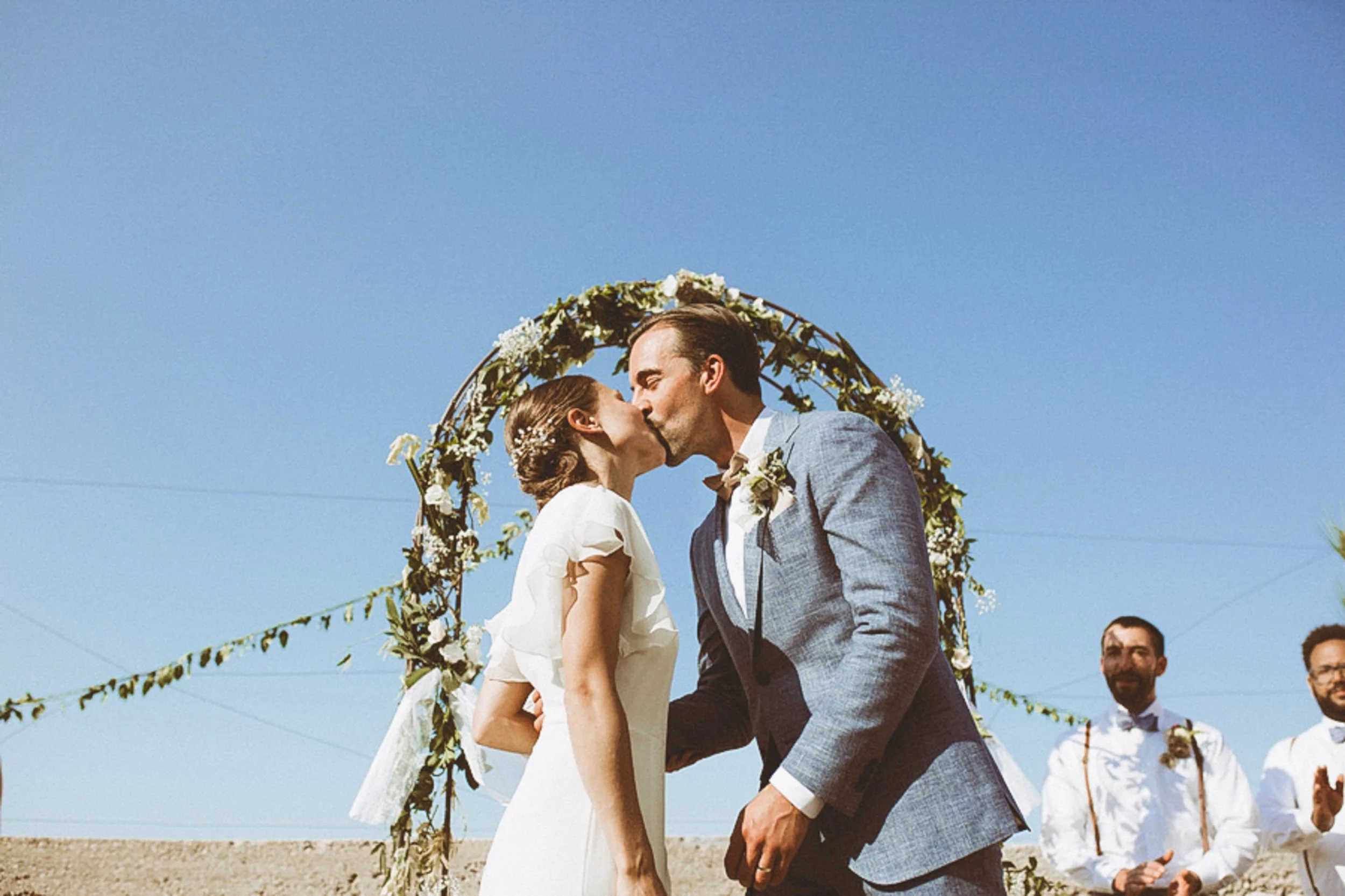 Bride and groom kiss under a floral arch during their outdoor wedding ceremony in the south Bay.