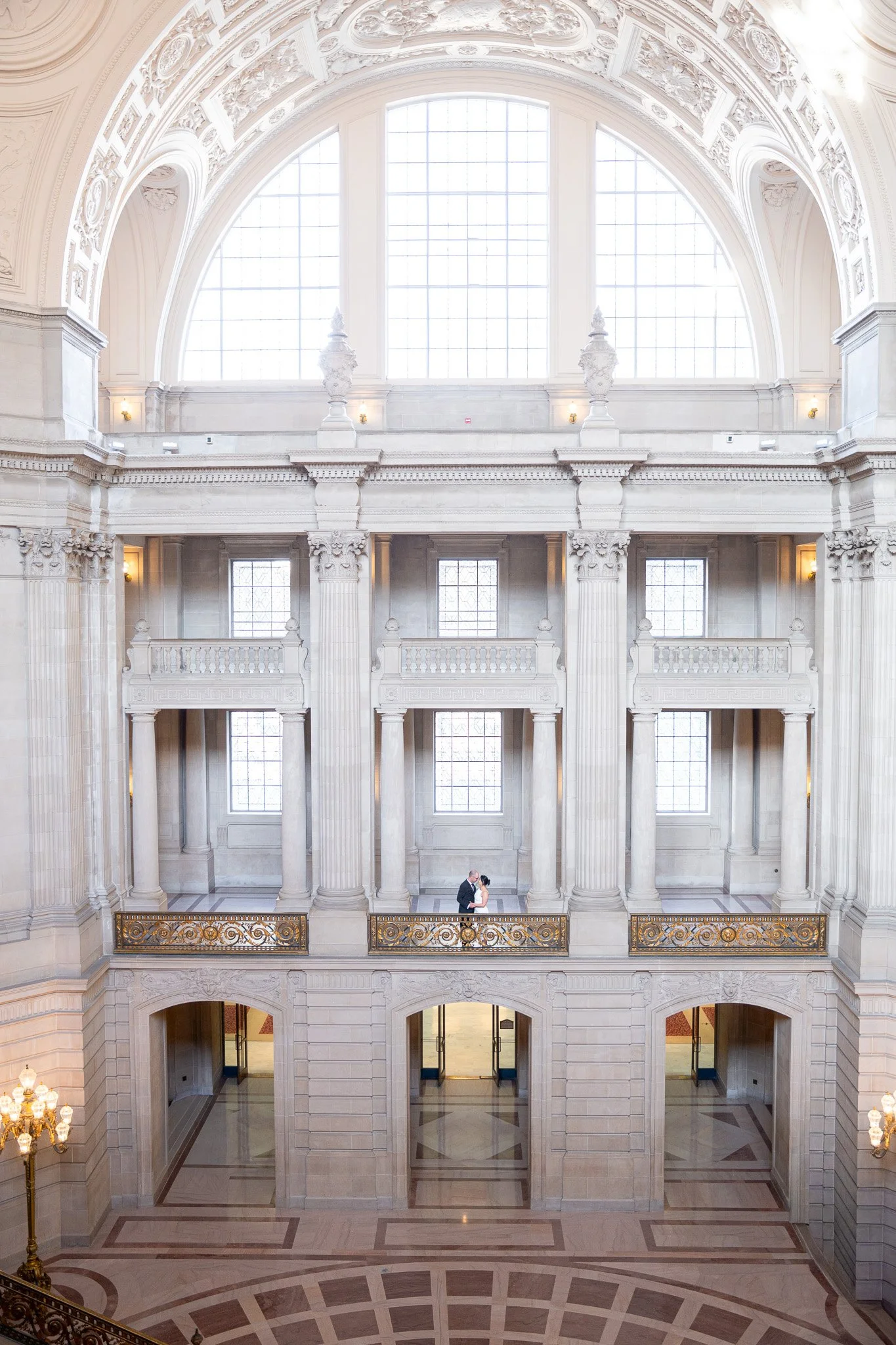 Couple standing in a grand, ornate lobby with tall columns and large windows, inside SF City Hall 1 Dr Carlton B Goodlett Pl, San Francisco, CA 94102.