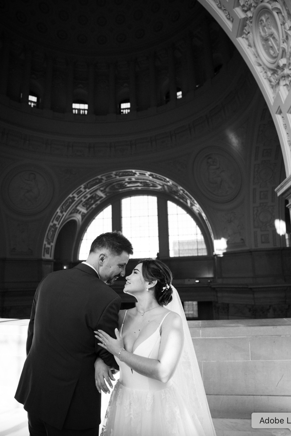 Black and white photo of a bride and groom standing closely inside San Francisco City Hall.