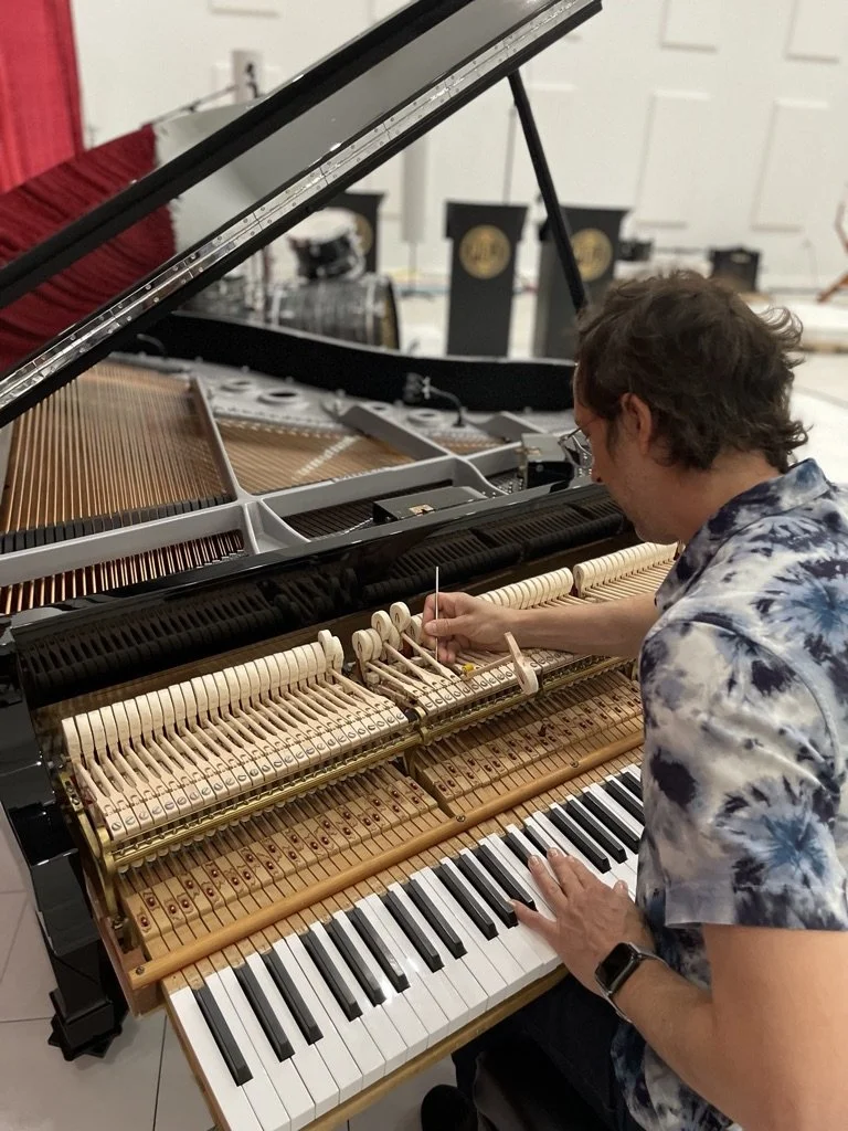 Man regulating the action of a grand piano with the lid open, showing the strings and hammers.