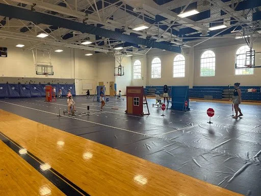 Children and adults playing in a gym with various sports equipment and decorations.