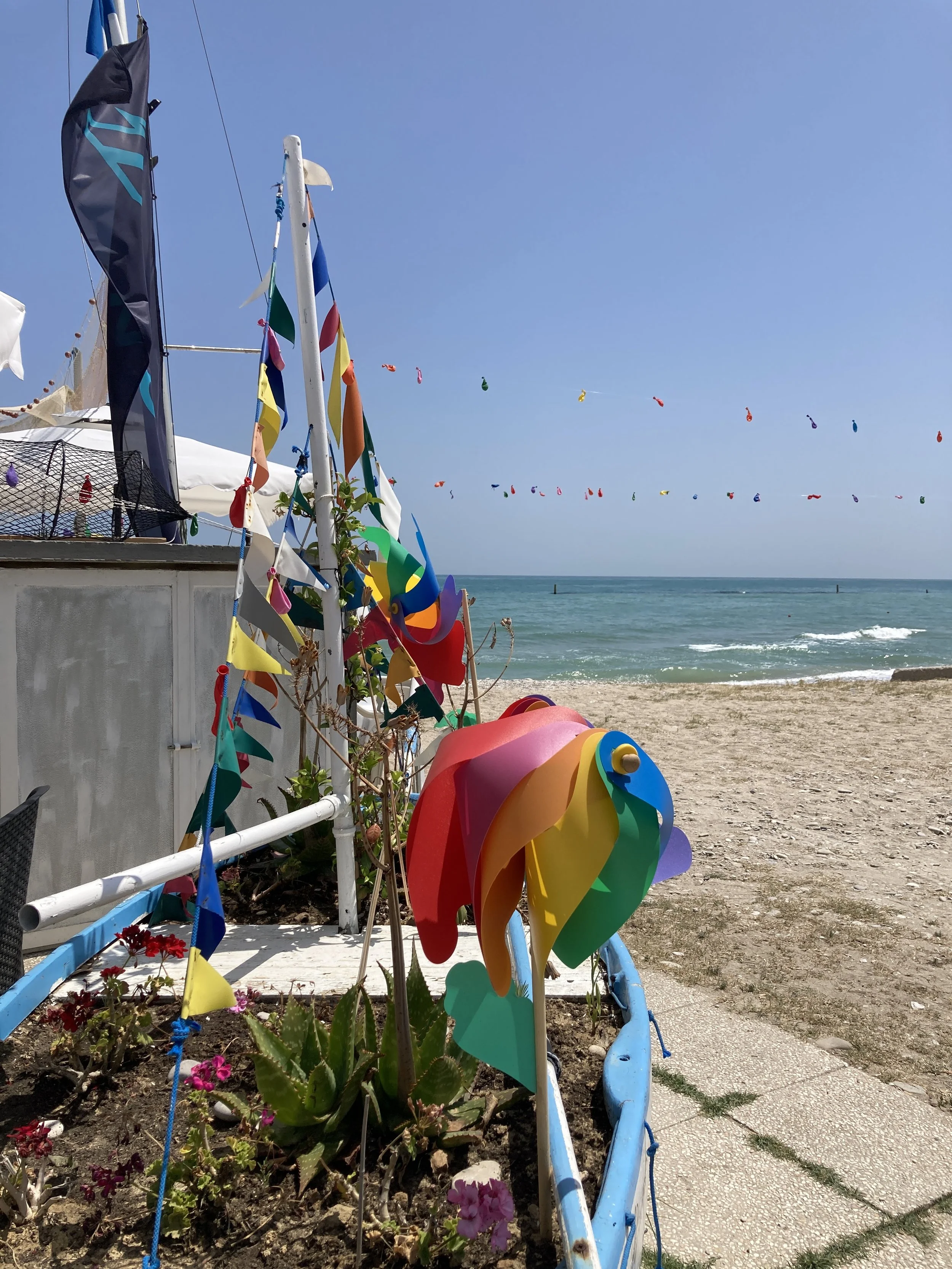 Colorful windmills and flags on a beachside patio with the ocean in the background.