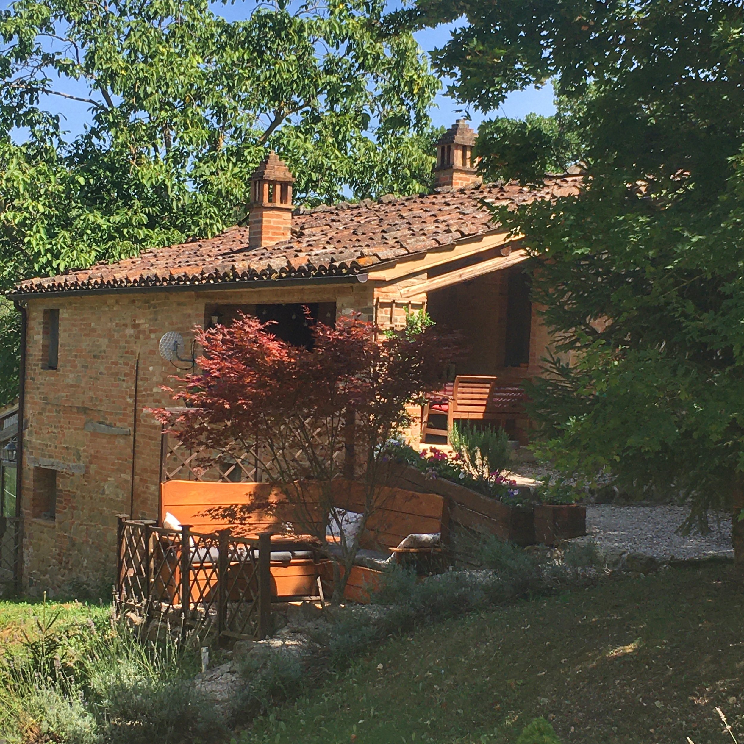 A brick house with a tiled roof, surrounded by green trees and plants, in a garden setting.