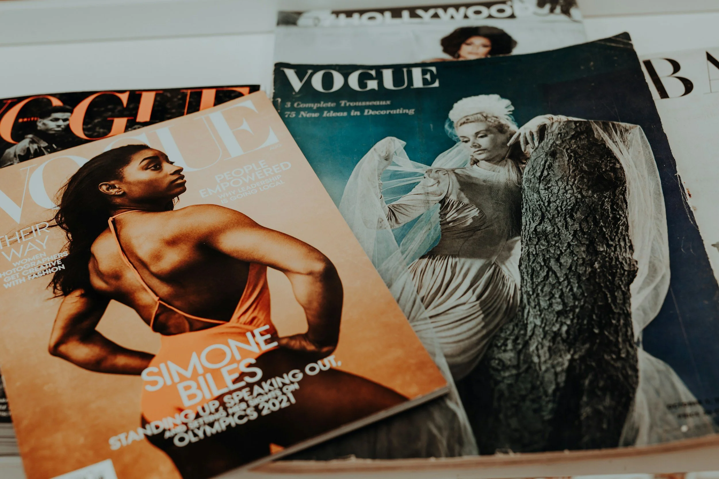 Plusieurs magazines de mode et de culture, notamment Vogue, Elle et Vogue, sont empilés sur une surface, avec une photo d'une femme noire en maillot de bain en premier plan sur le magazine Elle.