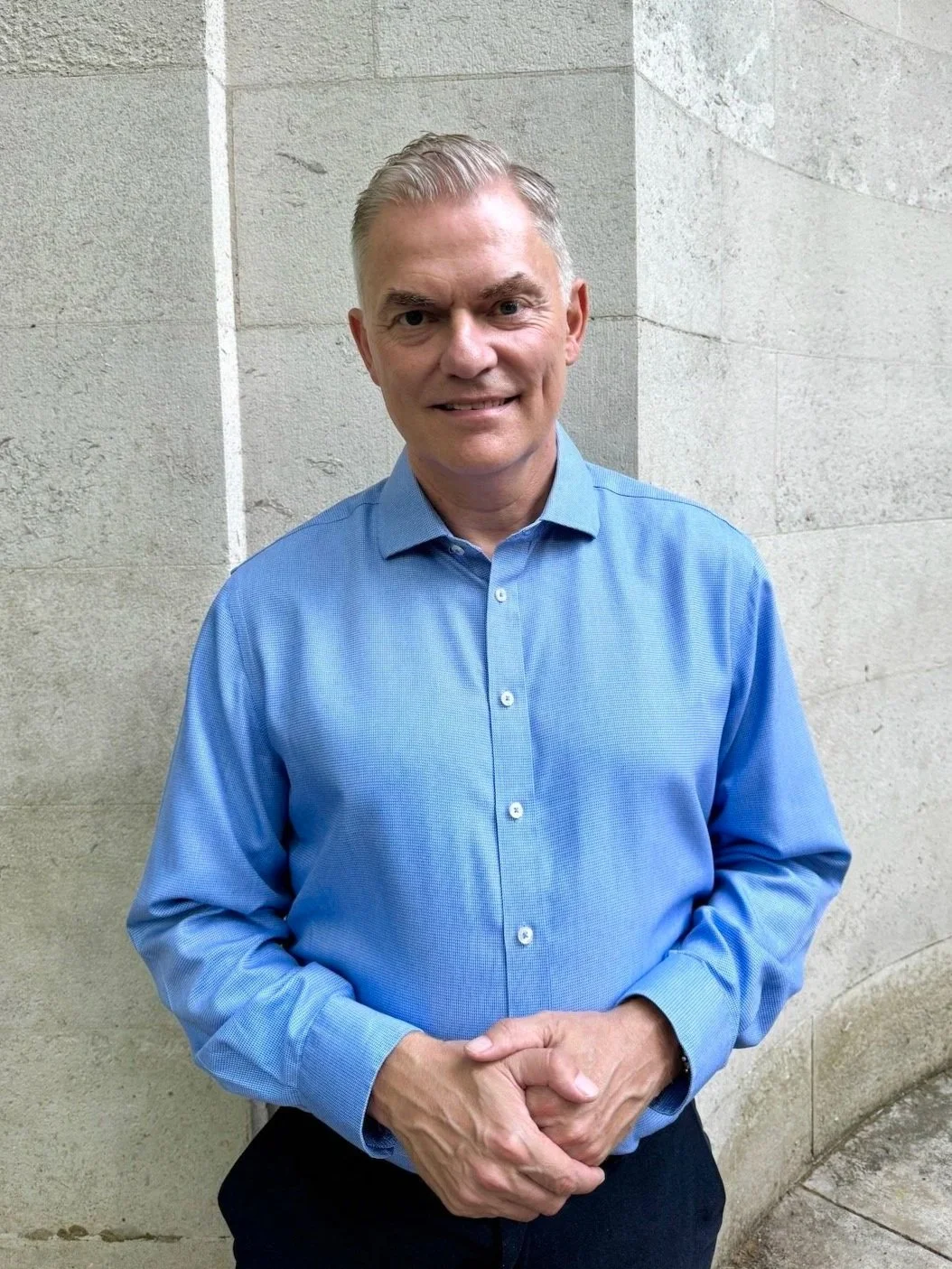 Jakob Holm smiling standing against a wall with hands clasped