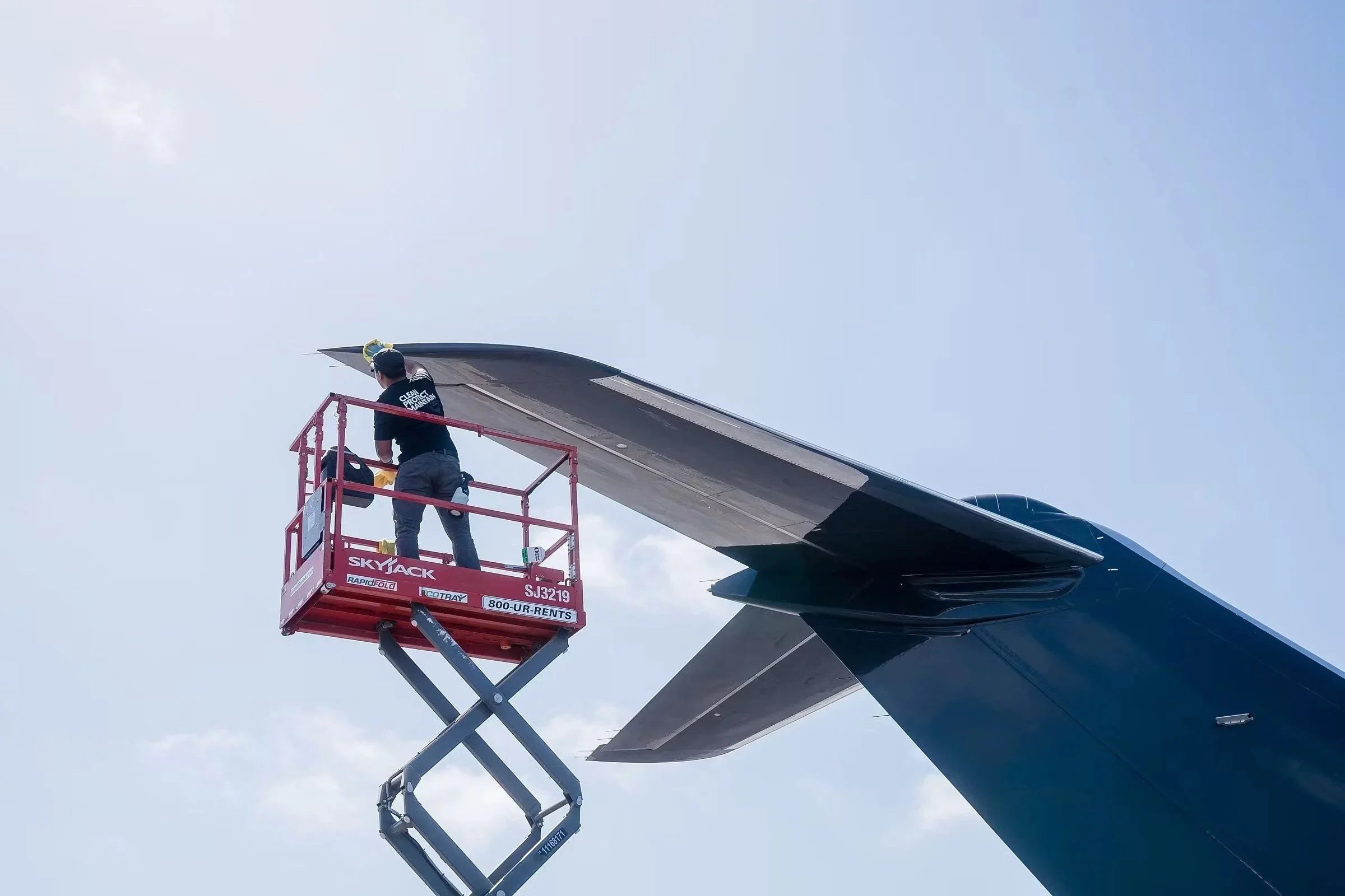 A person working on the wing of an aircraft while standing on a cherry picker lift against a cloudy sky.