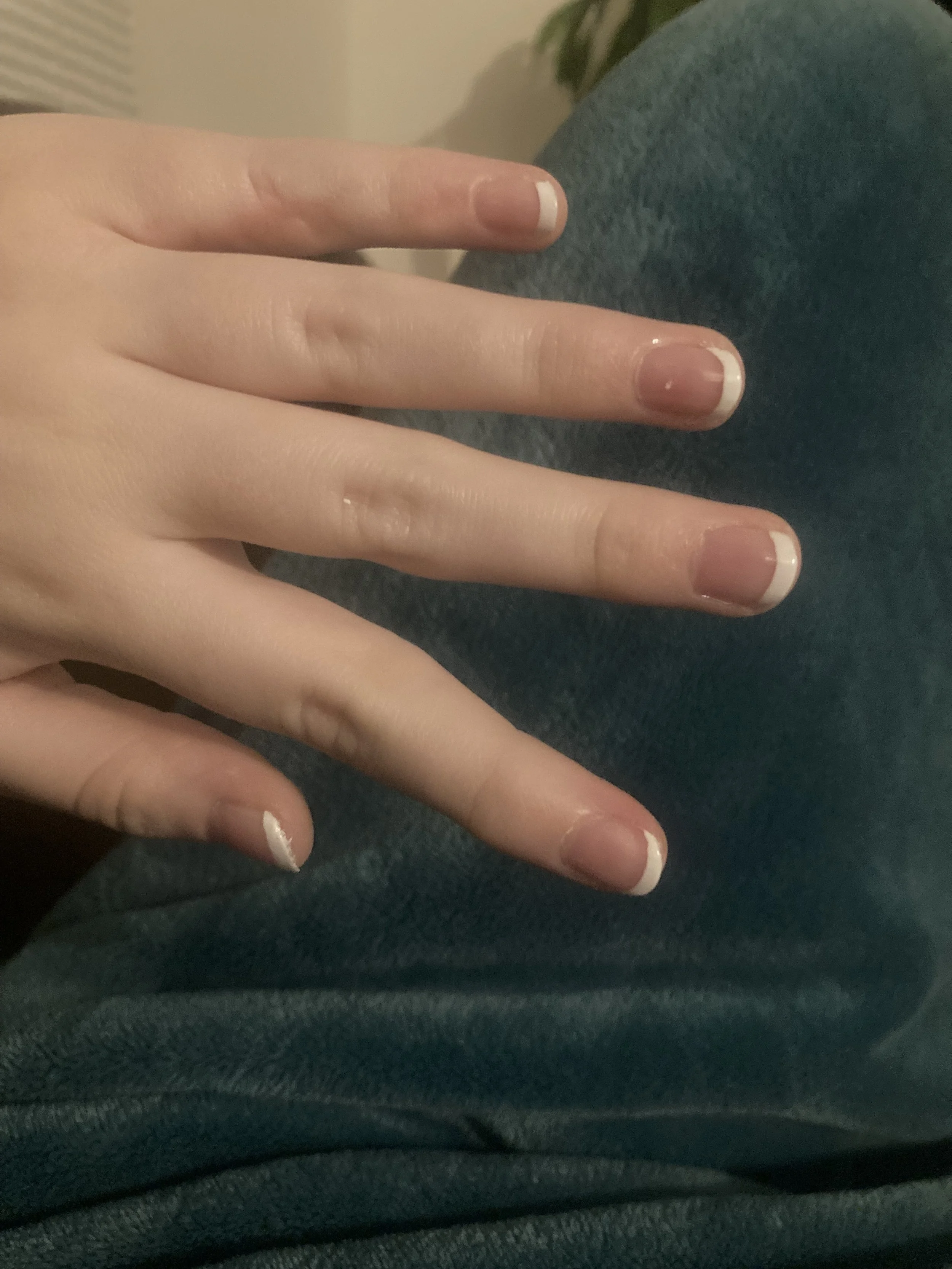Close-up of a person's hand with three fingers visible, showing neatly manicured nails with French tips, resting on dark fabric.