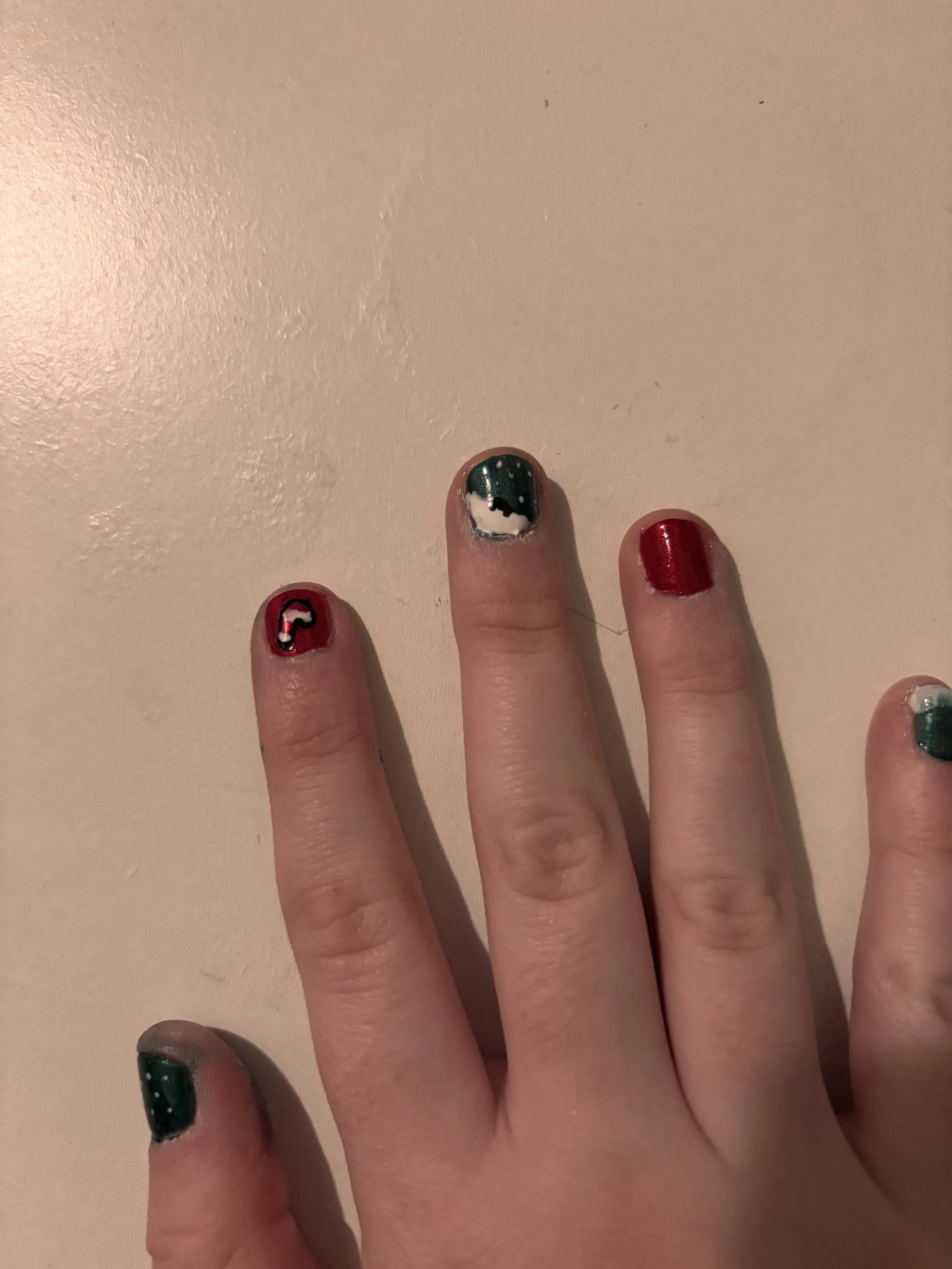 Close-up of a hand with painted nails, the middle finger has Christmas-themed nail art with a Santa hat, snowman's face, and Christmas lights on a red, green, and white background.