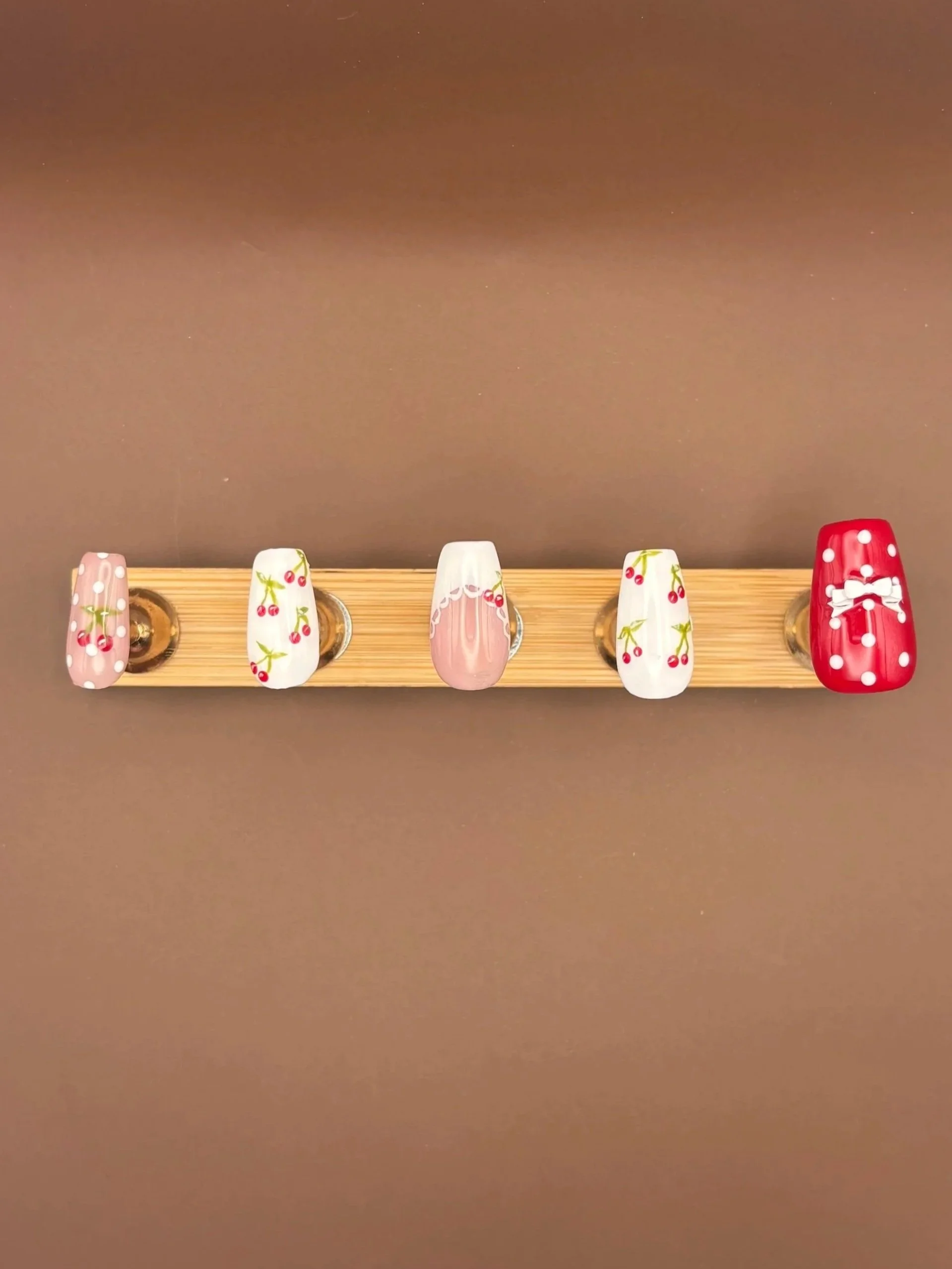 A wooden display with five decorated ceramic cups, each featuring a cherry pattern, on a brown background.