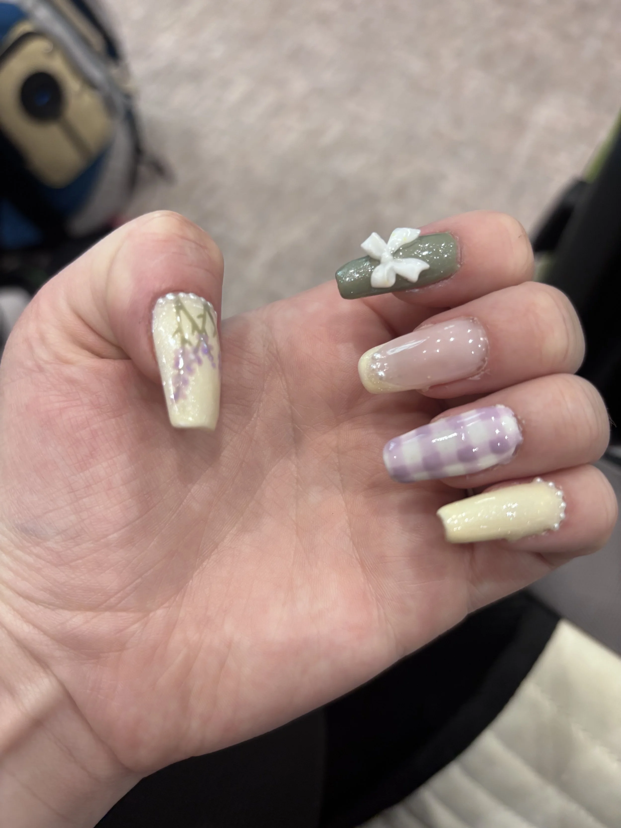 Close-up of a person's hand showing decorated fingernails with various pastel and floral designs.