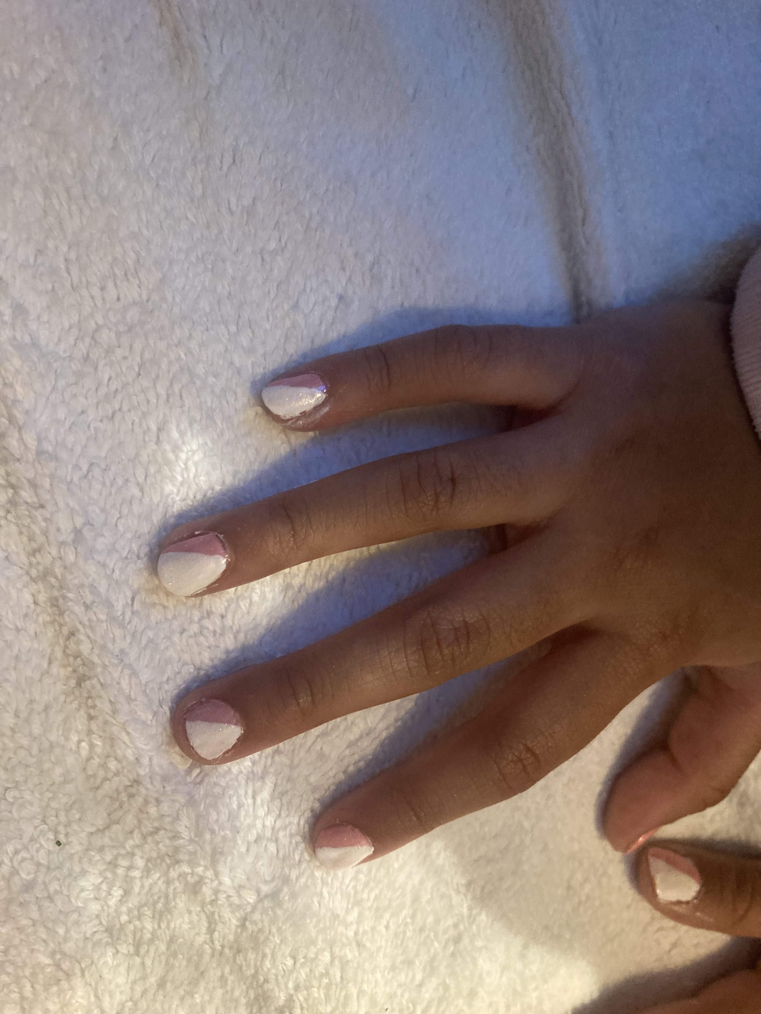 Close-up of a person's hand with fingers spread, showing white and pink nail polish on short nails, resting on a white textured surface.