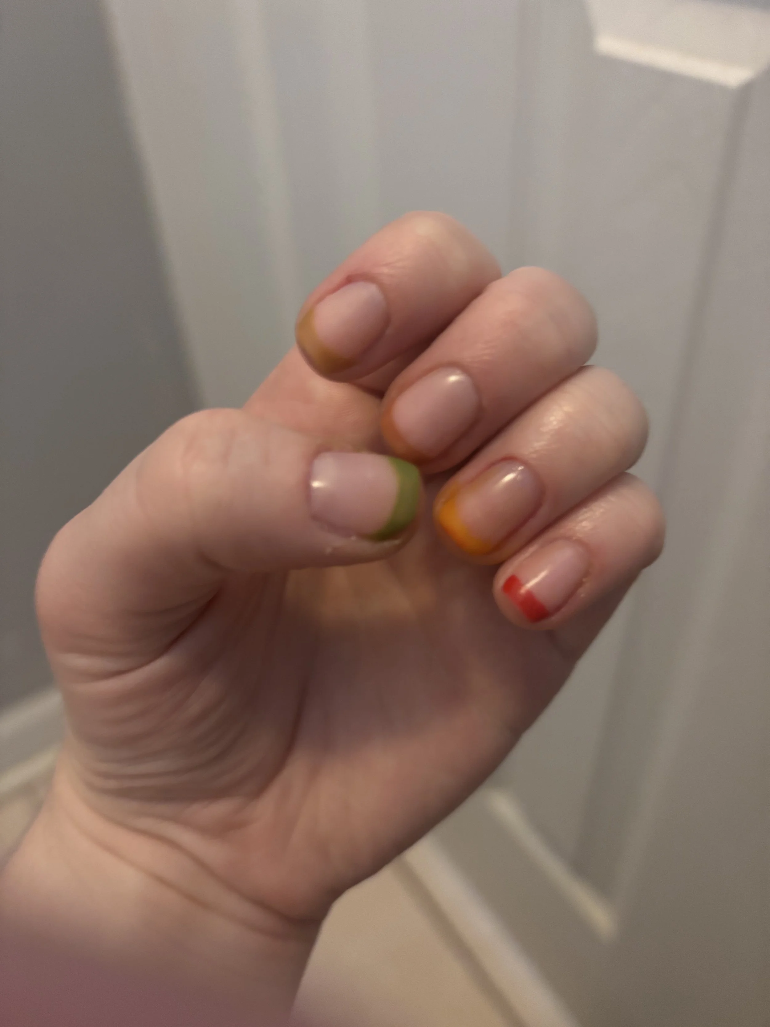 Close-up of a person's hand with multicolored painted nails, with a blurred beige and white background.