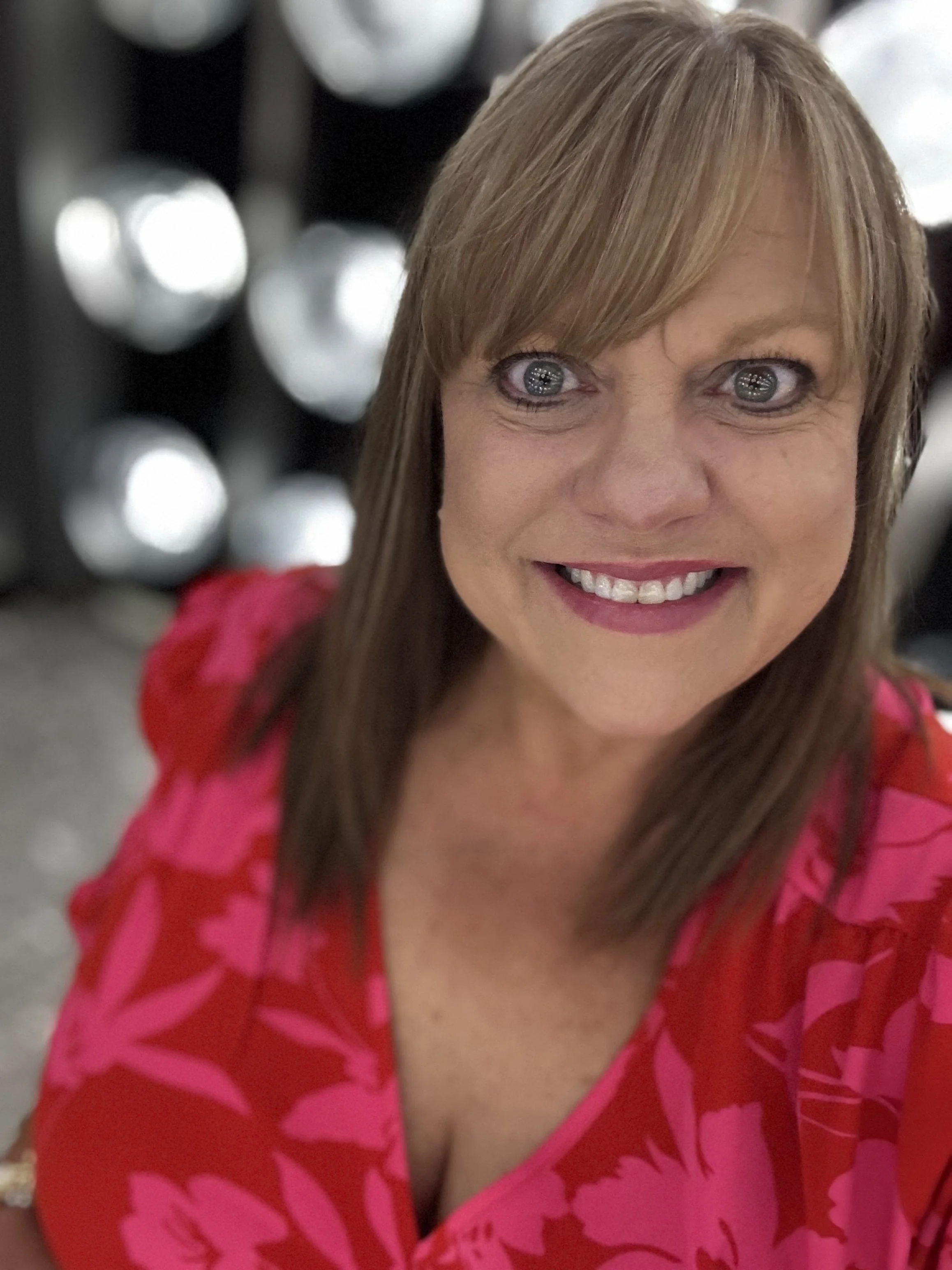 Close-up of a woman smiling on a cruise, wearing a bright pink dress with floral patterns, with blurred background.