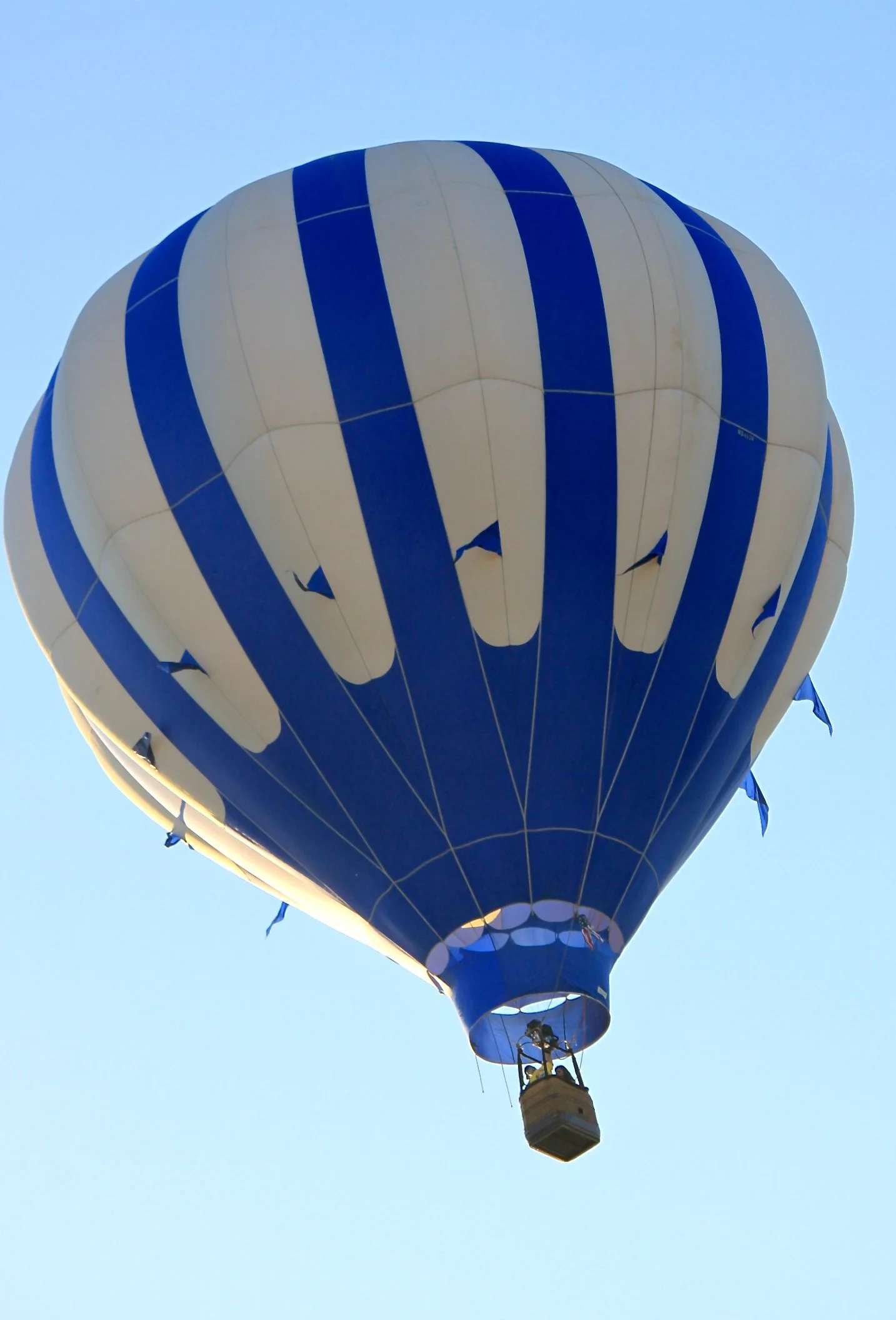 A hot air balloon with blue and white vertical stripes flying in a clear blue sky, flying over the Napa Valley, Napa CA